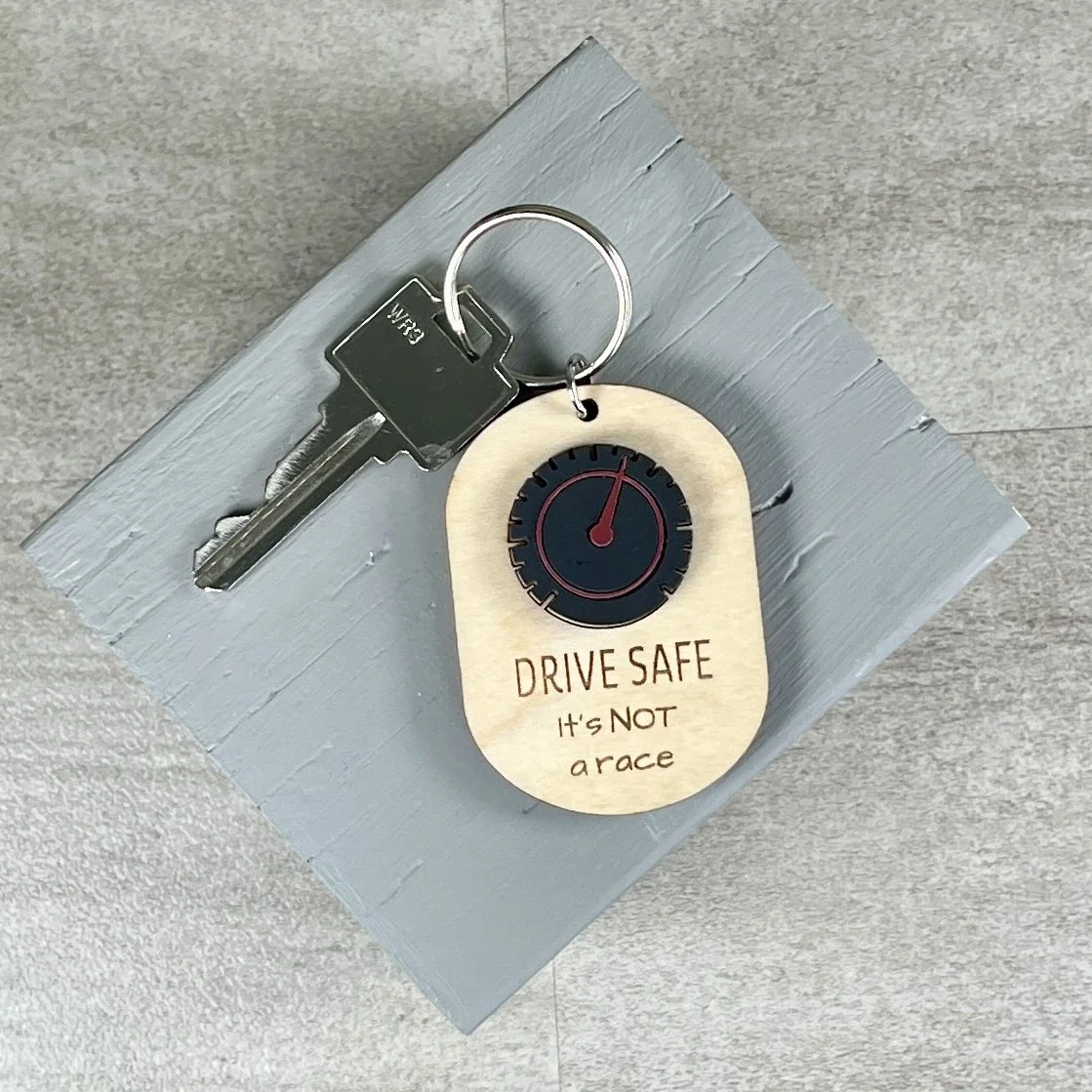 lifestyle shot of laser cut maple wood keychain with speedometer in matte black/red acrylic and the engraved phrase "DRIVE SAFE It's not a race".