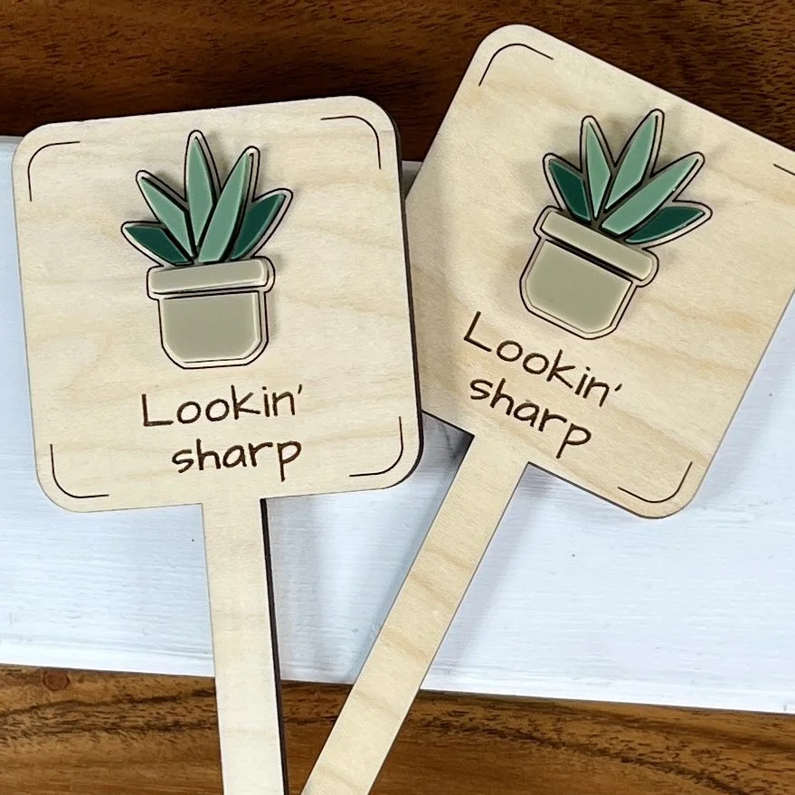 flat lay maple plant stake featuring a potted spider plant embellishment engraved with the phrase "Lookin’ sharp".