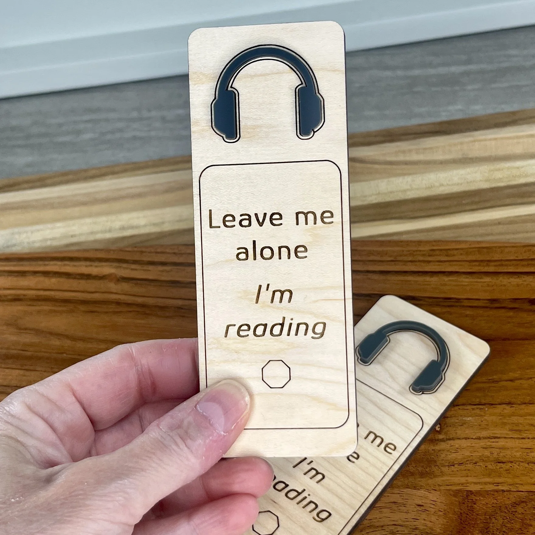 handheld maple bookmark featuring a charcoal grey acrylic headphones embellishment engraved with the phrase "Leave Me Alone I’m Reading".