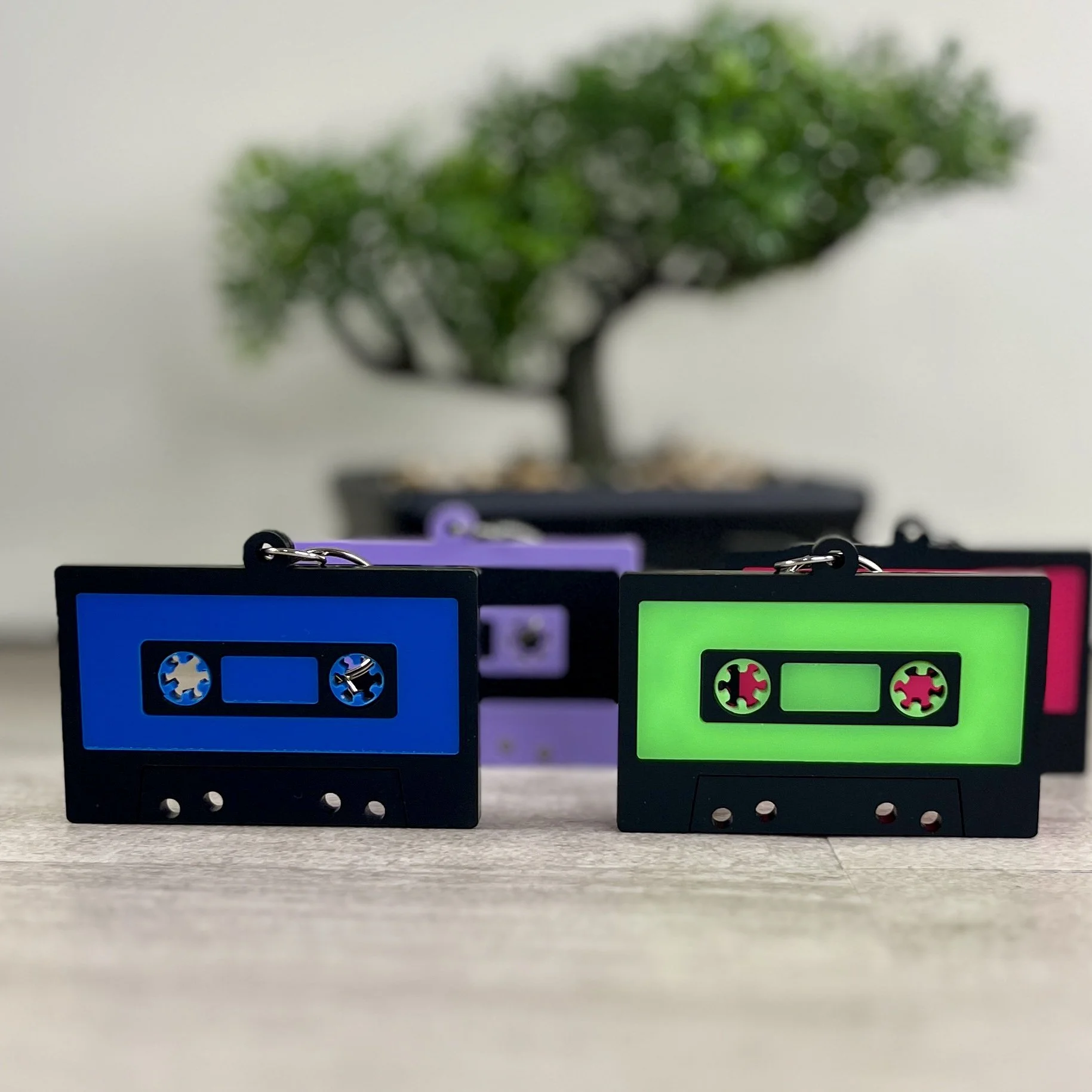 Retro cassette tape-shaped acrylic backpack tags in purple and radioactive green, available with personalized names.