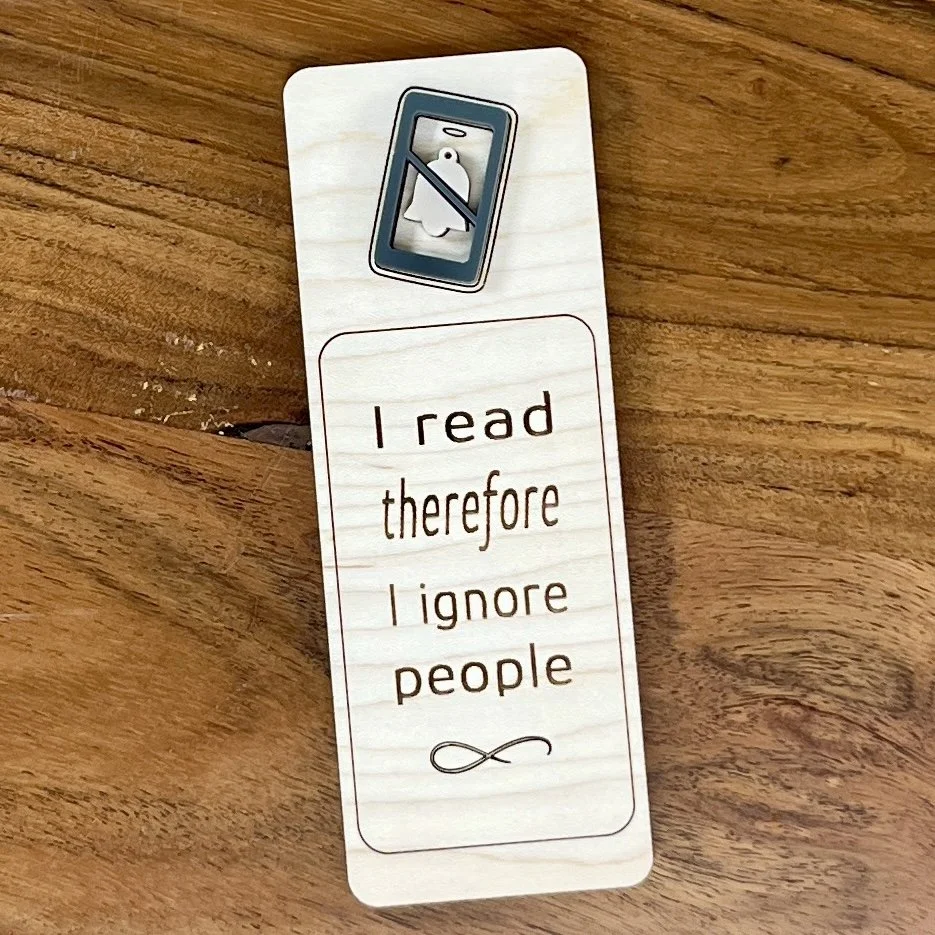 flat lay maple bookmark featuring a blue acrylic do not disturb symbol embellishment engraved with the phrase "I read therefore I ignore people".