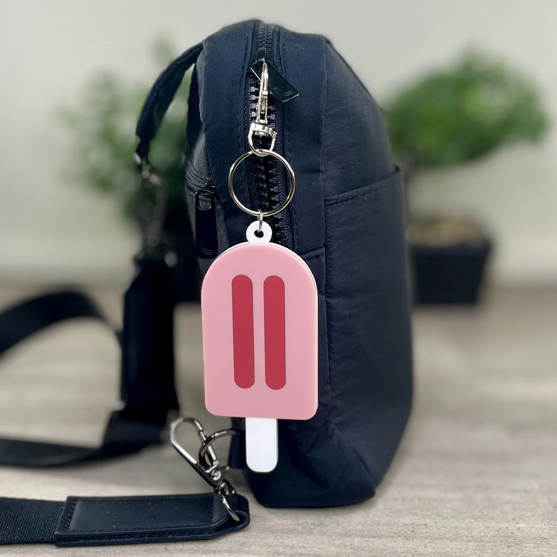 Popsicle-shaped pink acrylic backpack tags hanging from bag.