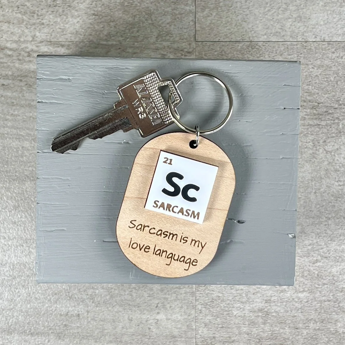 lifestyle shot of maple wood keychain with a periodic table-inspired acrylic tile reading "Sc" for Sarcasm and the engraved phrase "Sarcasm is my love language."