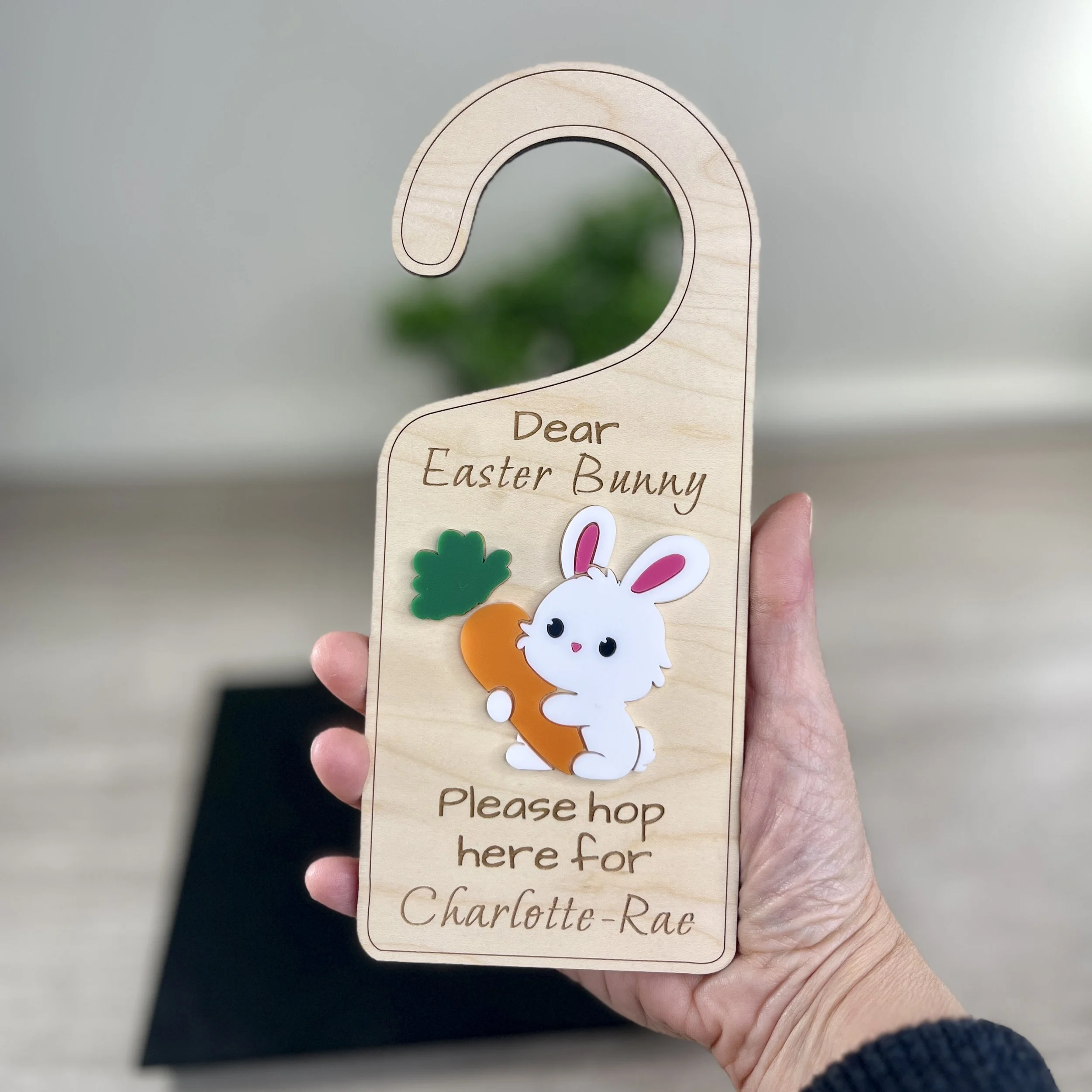 Laser cut maple wood Easter bunny door hanger with raised Easter bunny graphics held in hand for scale.