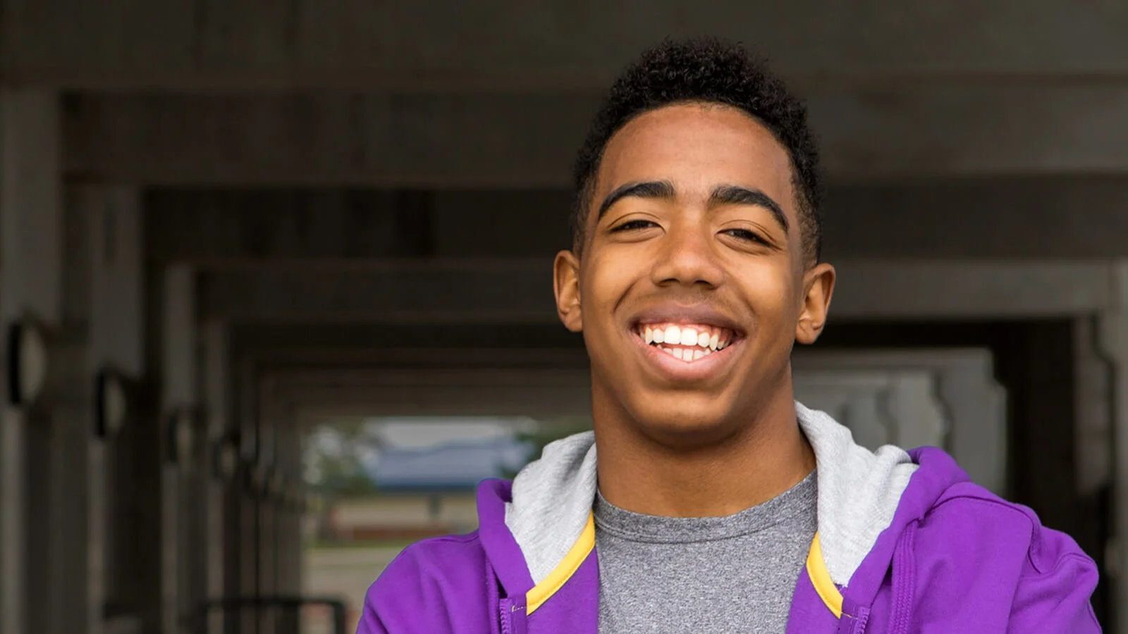 Grace Place student in purple sweatshirt smiling confidently, representing success through mentorship, education, and job readiness programs.