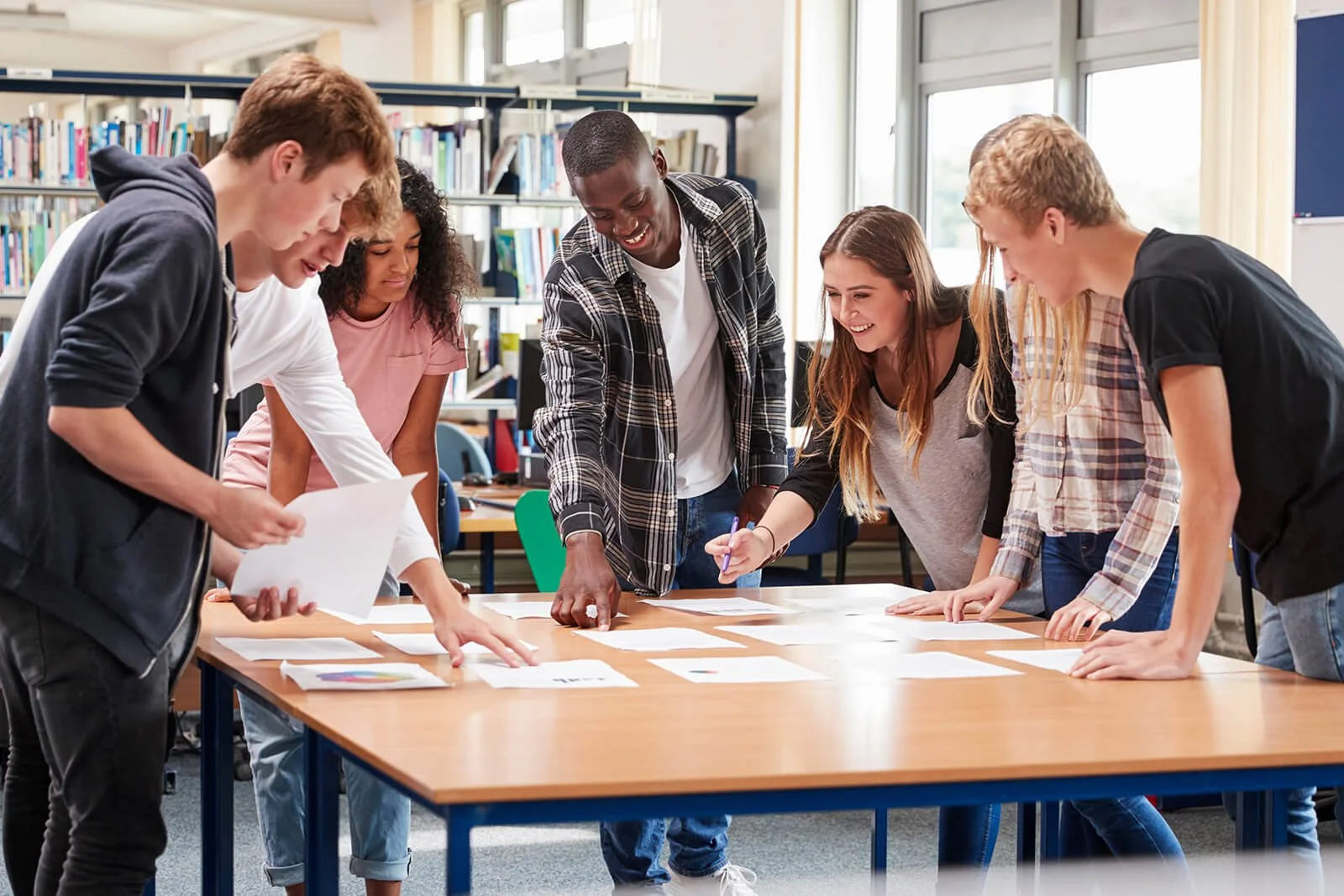 Group of diverse teens collaborating around a table, symbolizing community support and the impact of taking action through volunteering and giving.