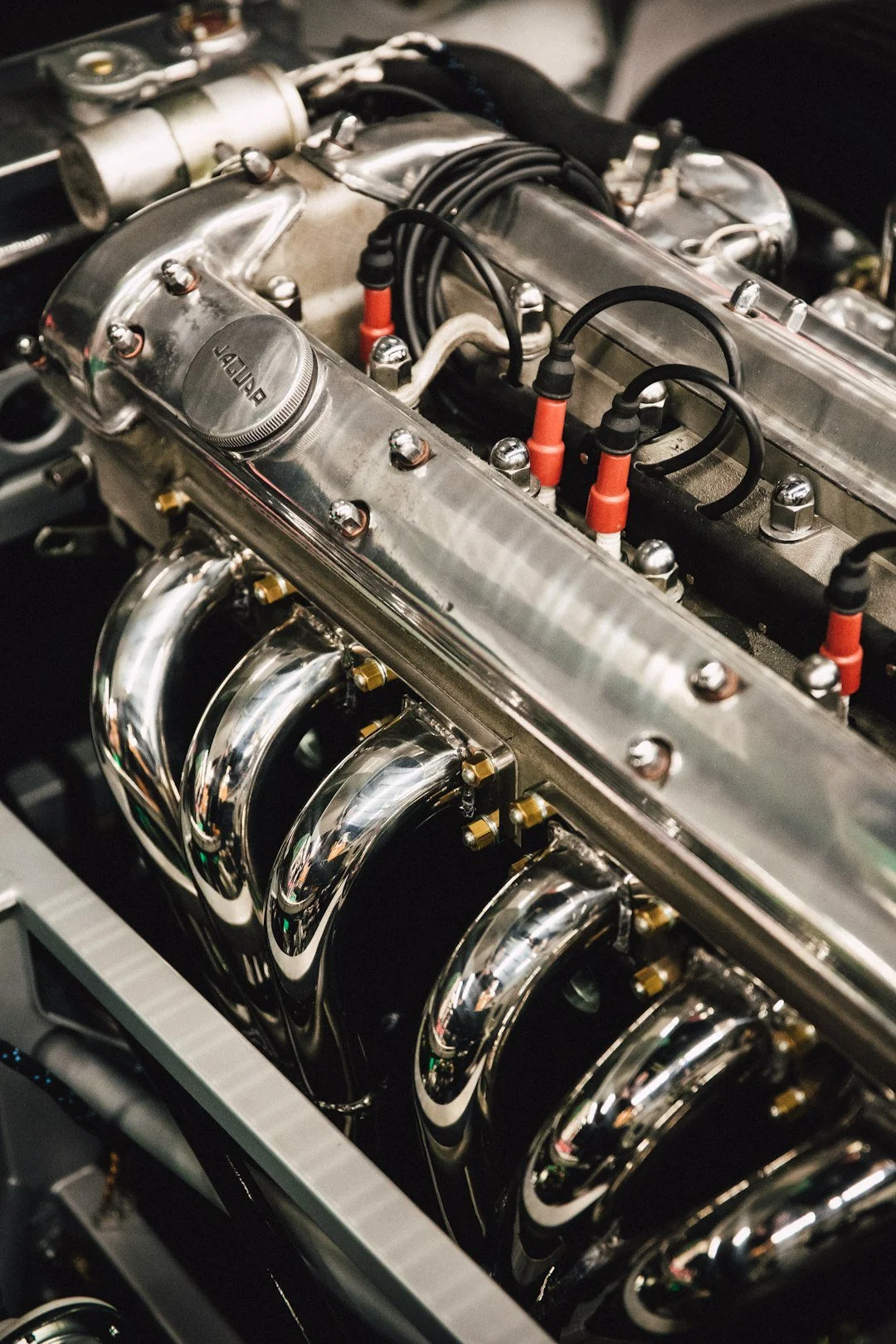Close-up of a polished chrome car engine with visible exhaust manifold and red ignition wires.