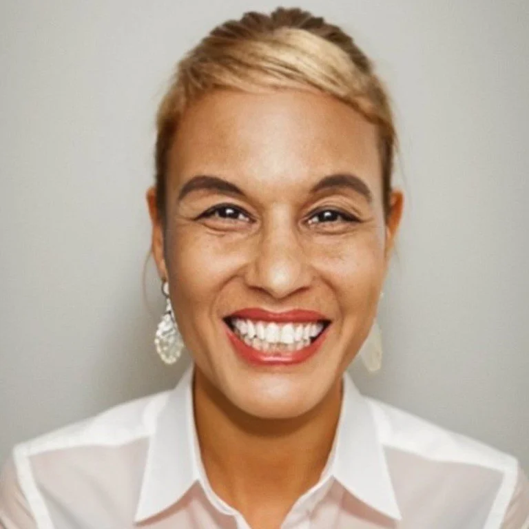 A woman smiling with short blonde hair, wearing a white shirt and large earrings.