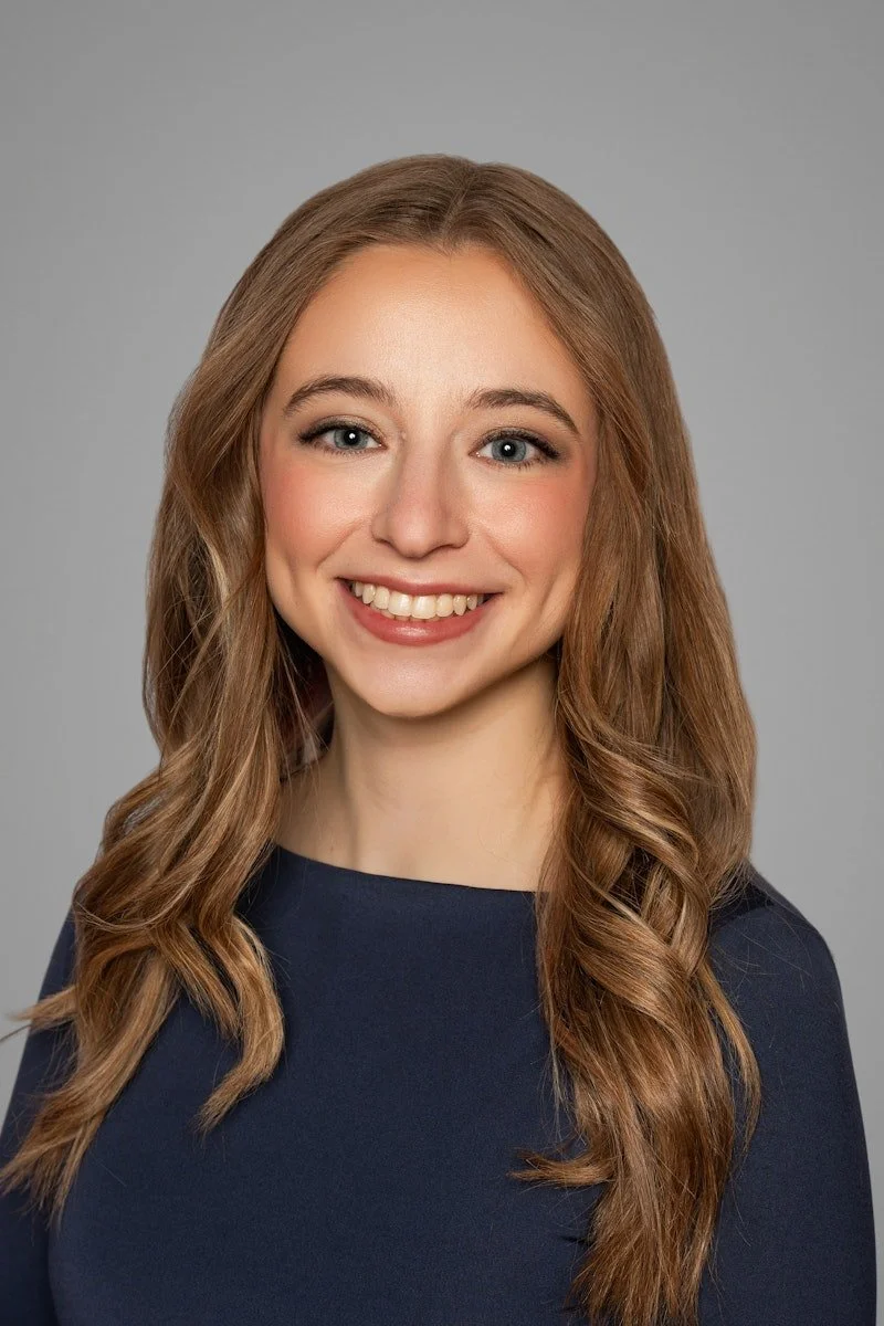 Headshot of a neurodivergent-affirming therapist in Cincinnati, OH, with long, wavy, light brown hair, wearing a navy blue top, smiling against a gray background.