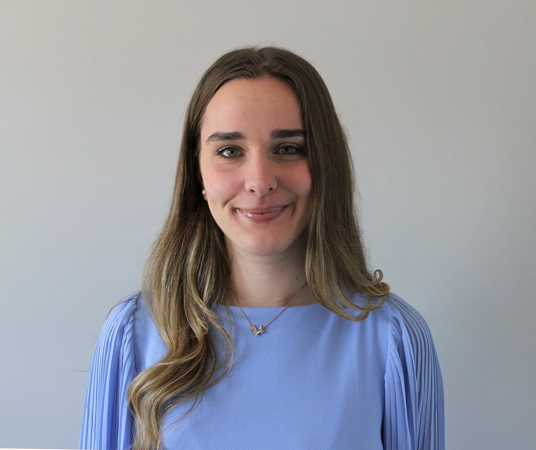 A woman neurodivergent-affirming social worker, in Cincinnati, OH, with light skin, long wavy hair, blue eyes, wearing pearl earrings, a butterfly necklace, and a blue blouse with pleated sleeves.