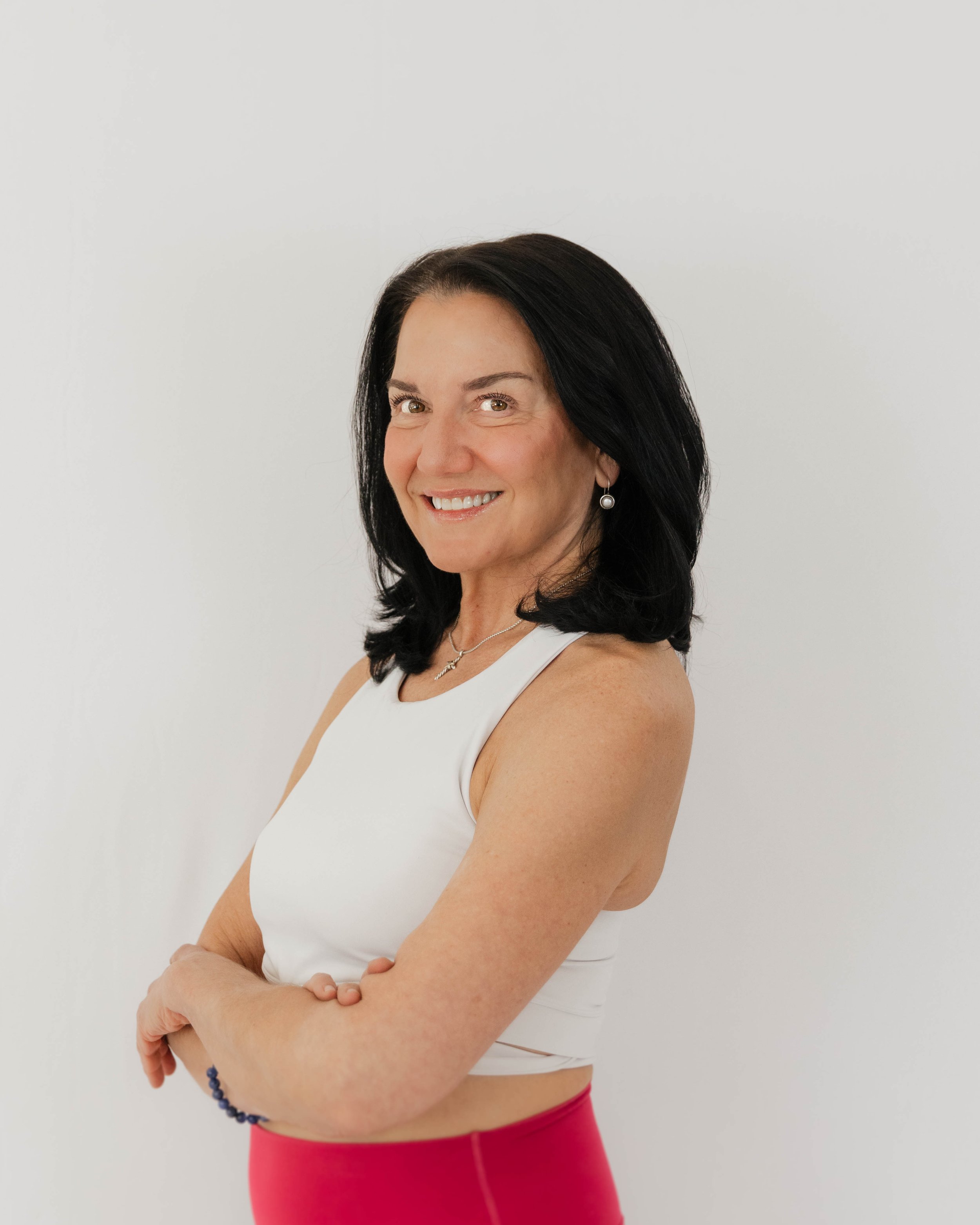 Photo of a smiling woman with black hair, wearing a white sleeveless top against a light blue background.