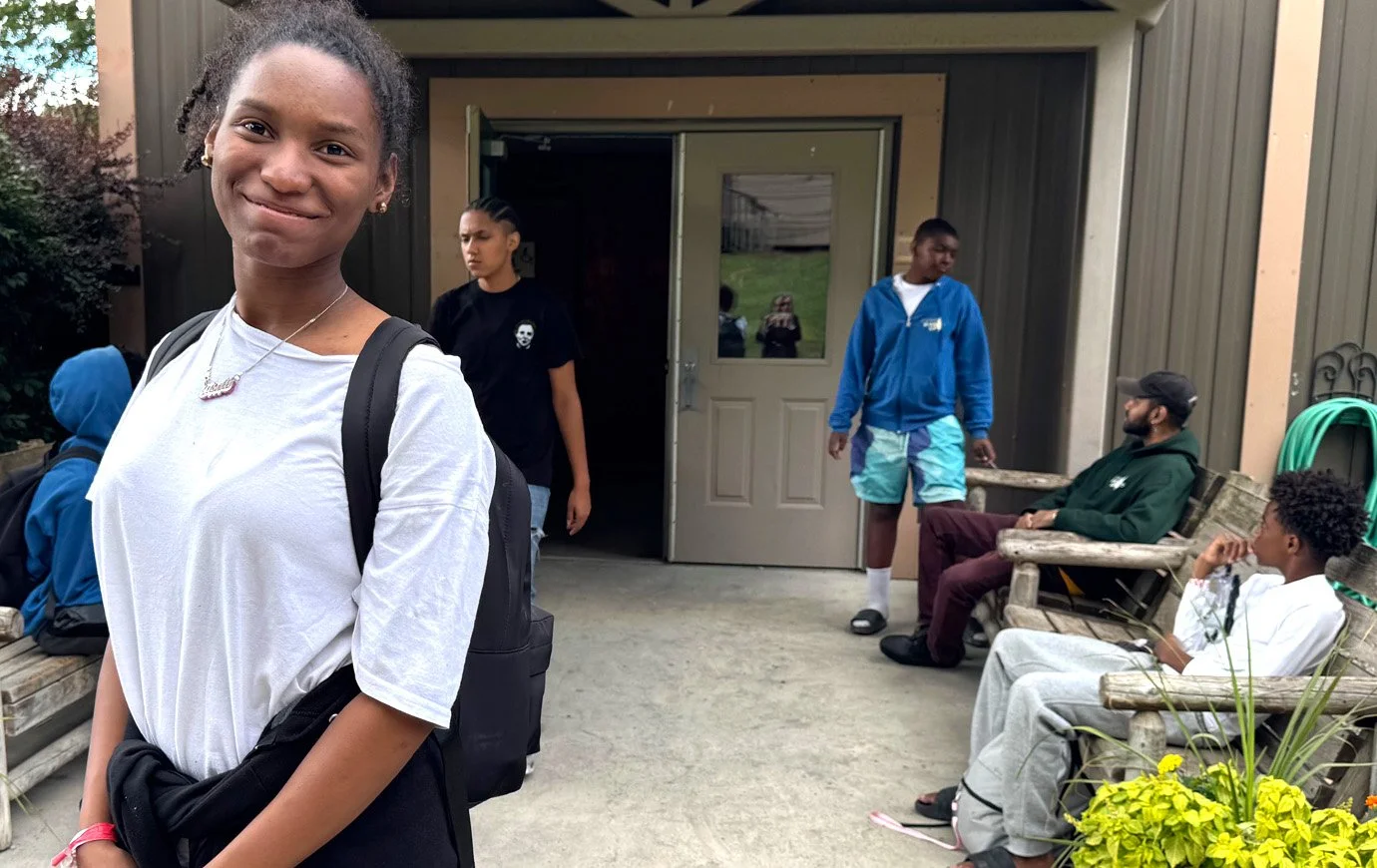 Girl in a white tee smiles for the camera outside one of the camp buildings