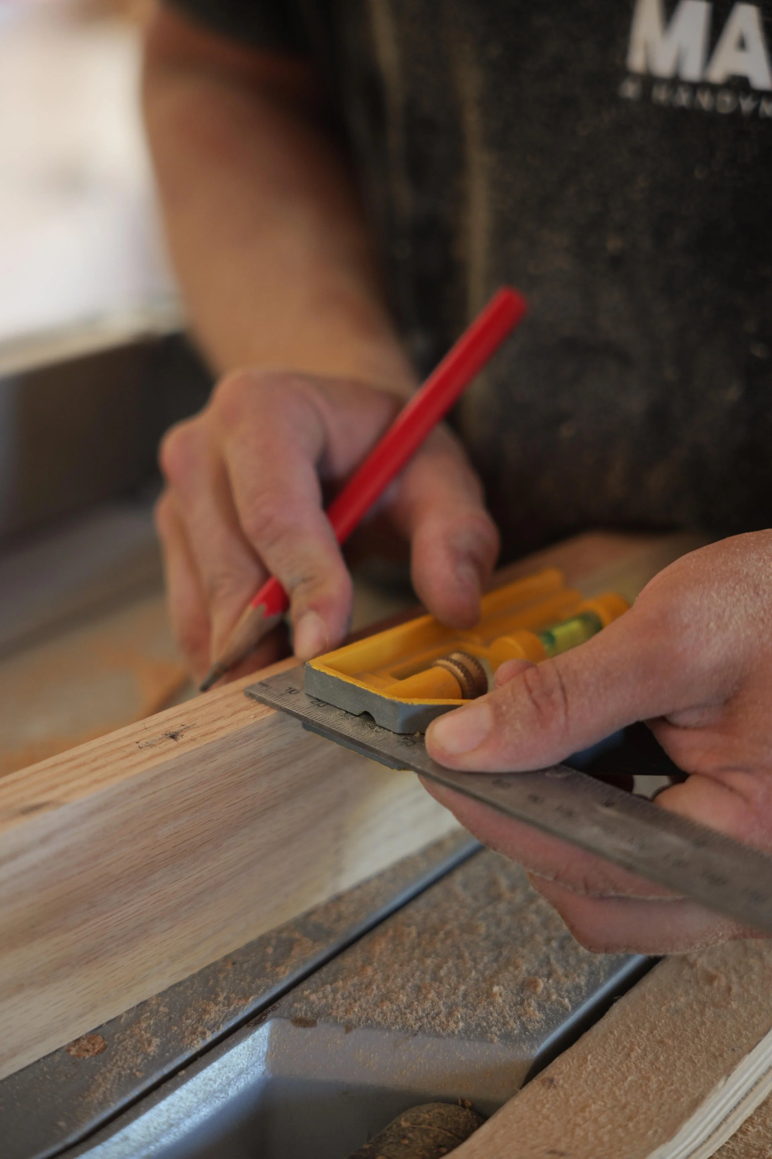 Hands using an adjustable square to mark precise measurements on a woodworking project during a ManMade workshop