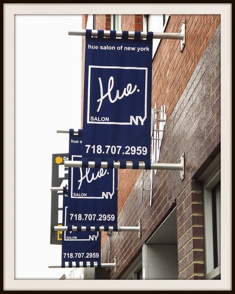 Exterior view of Hue Salon in New York with blue signs displaying the salon's name, logo, and phone number.