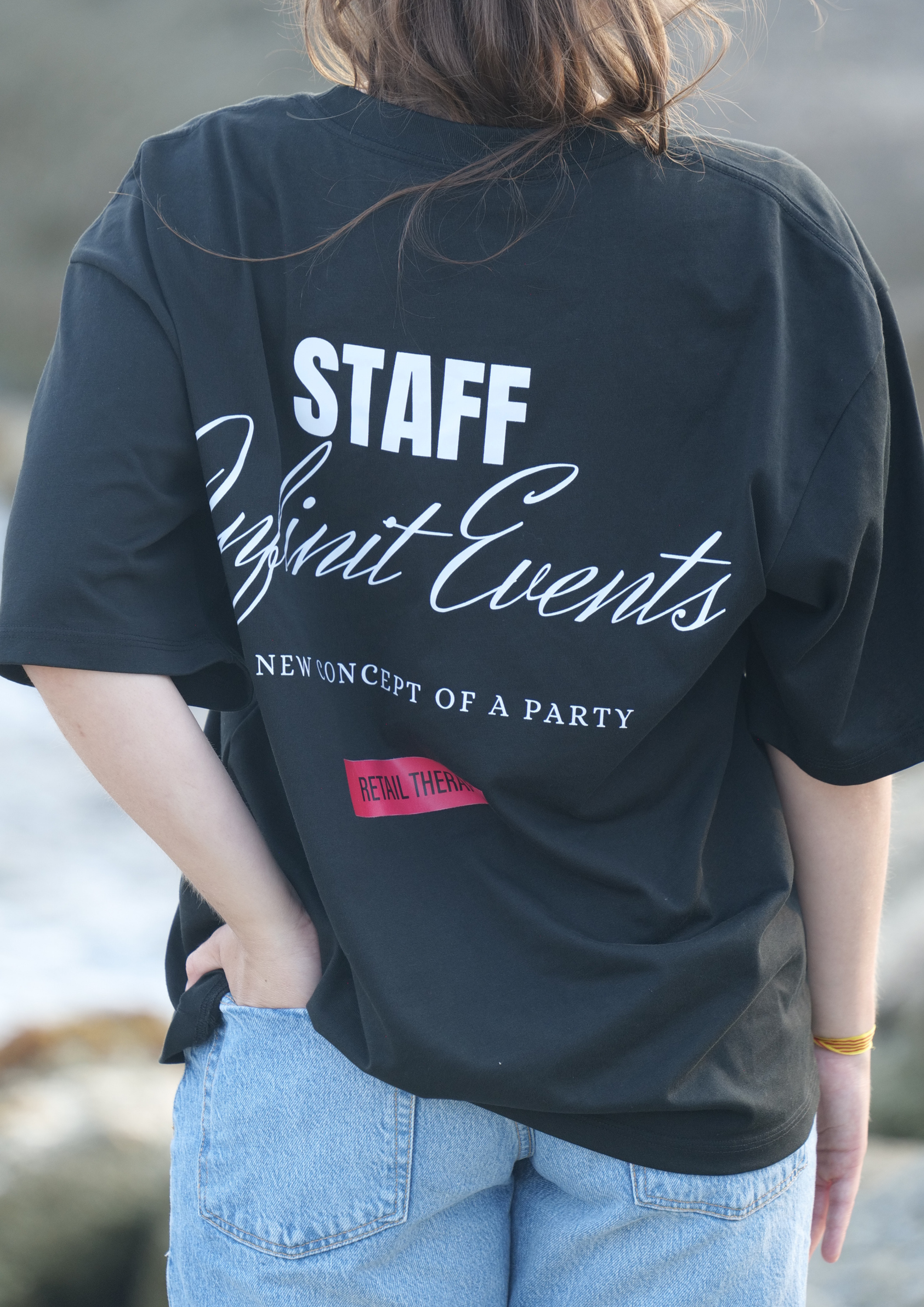 Persona de espaldas usando una camiseta negra con texto que dice 'STAFF' y 'Night Events' en letras blancas, y pantalones vaqueros azules claros.