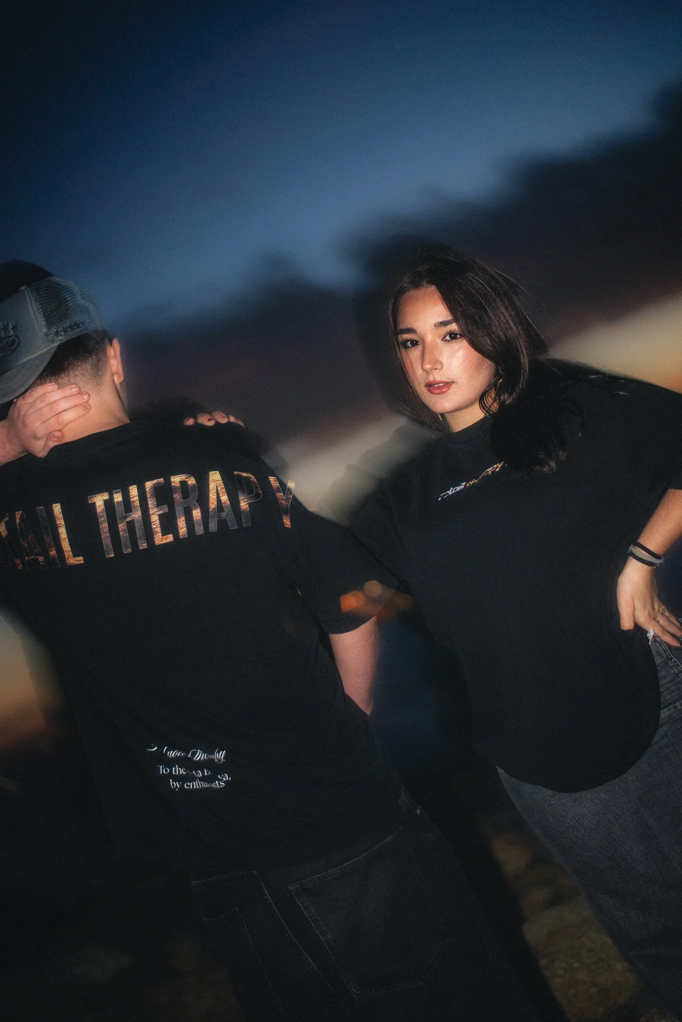 Mujer con cabello largo y oscuro posando en un fondo oscuro y nublado, vestida con camiseta negra, en un ambiente nocturno.