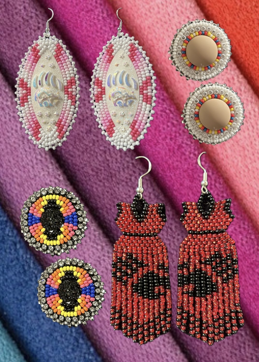 Colorful beaded earrings with various designs, including pink and white oval earrings, round earrings with rainbow bead patterns, and red and black beaded earrings shaped like ladybugs, all displayed on a multicolored fabric background.