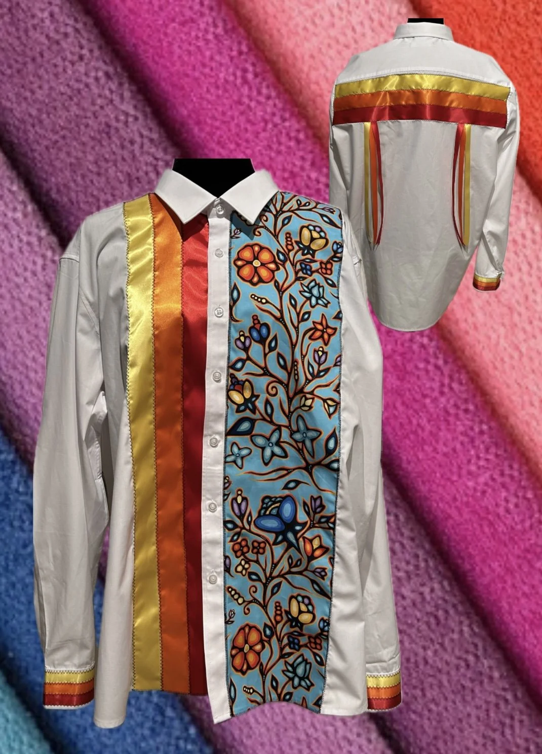 A white button-up shirt with colorful embroidered floral and butterfly patterns on the front panel, featuring vertical stripes in yellow, orange, and red on the left side and colorful embroidered cuffs, displayed against a multicolored knitted fabric background.