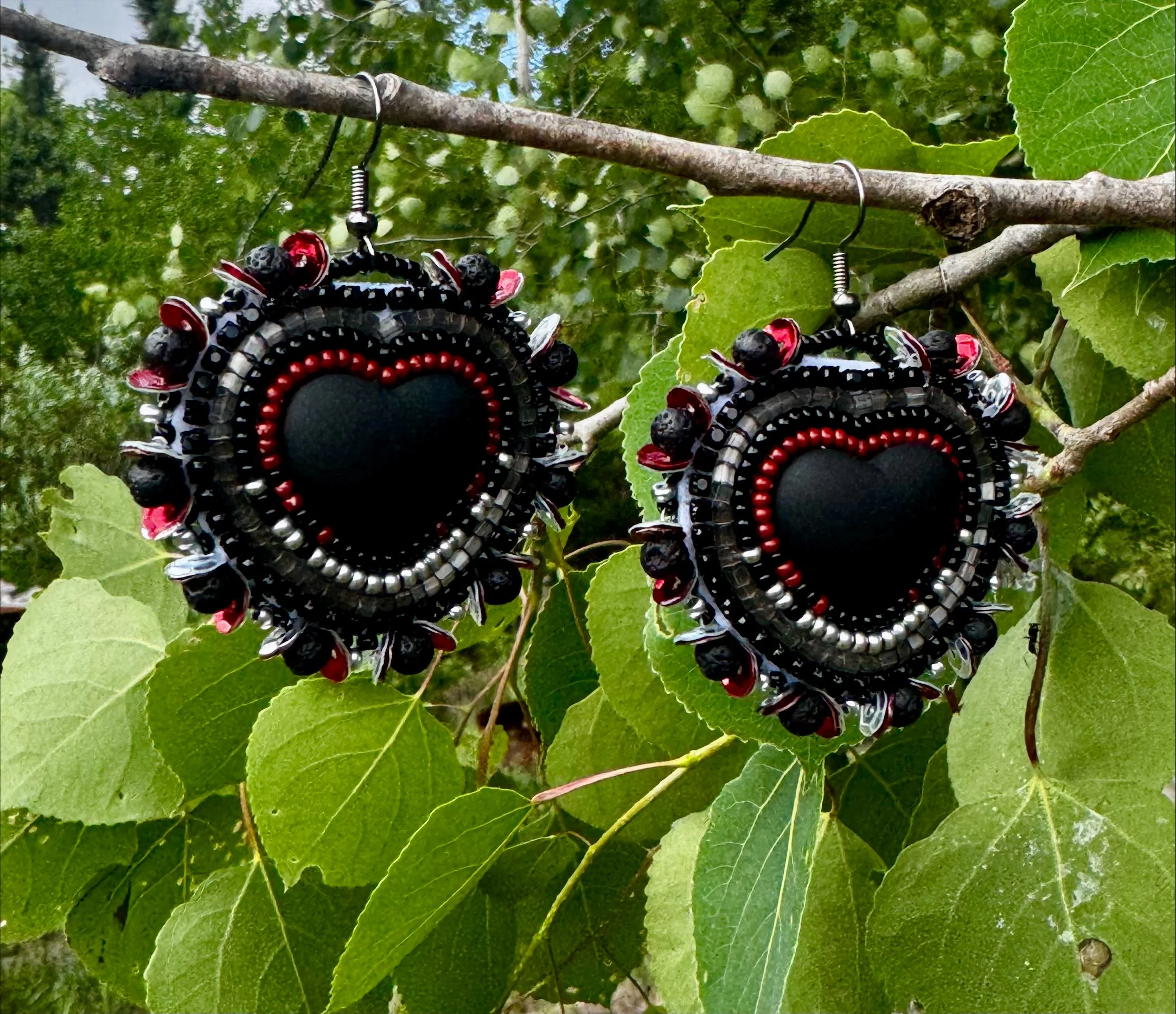 Colorful beaded earrings hanging from a tree branch with green leaves in the background.