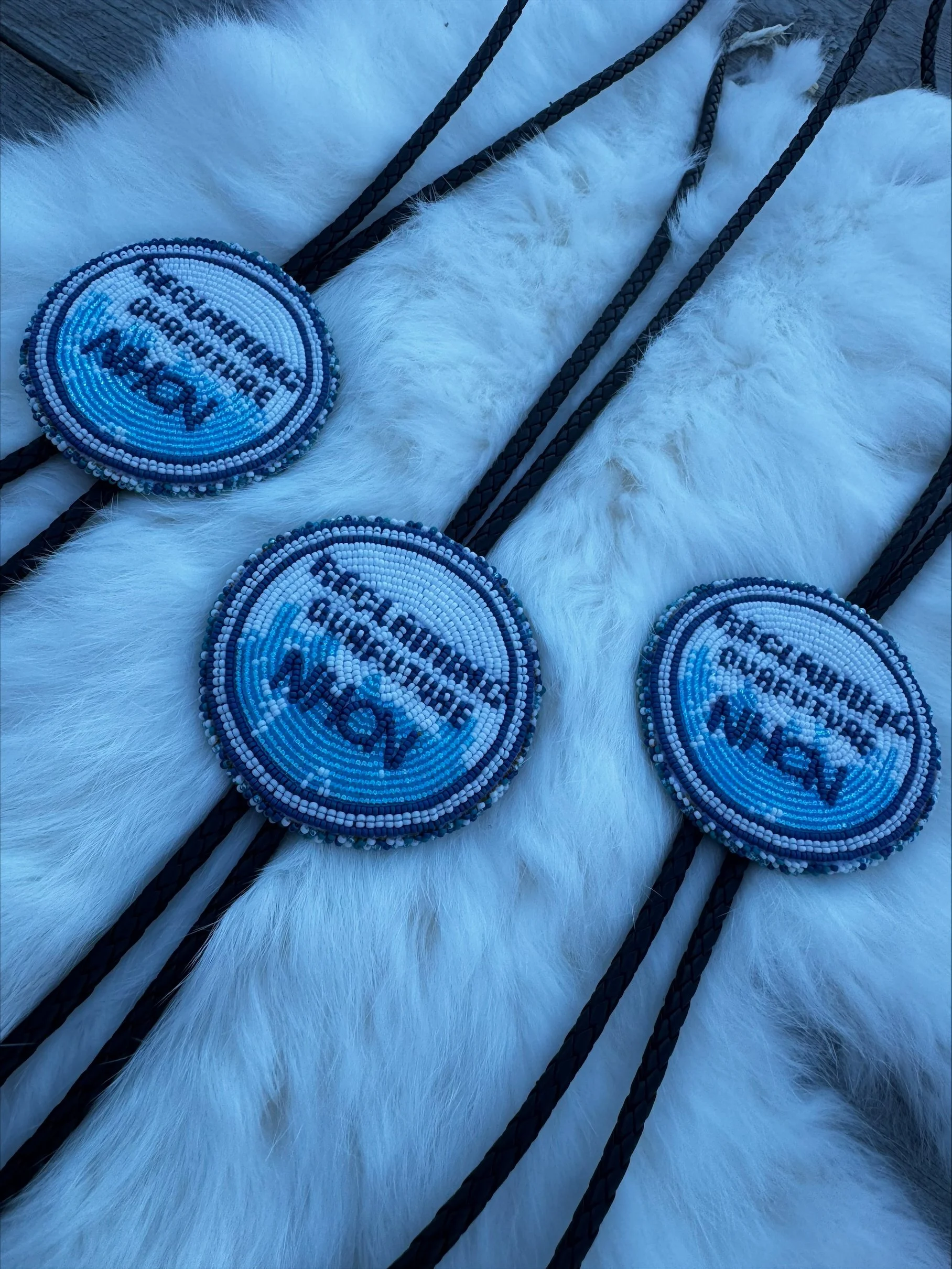Blue circular beaded items with the text 'WILD' and an animal silhouette, placed on white fur and intersected by black ropes.