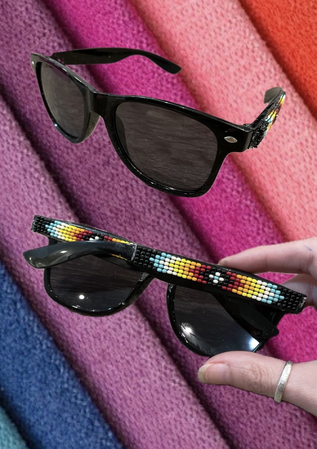 Two pairs of black sunglasses with decorative beaded arms, set on colorful tweed fabric.