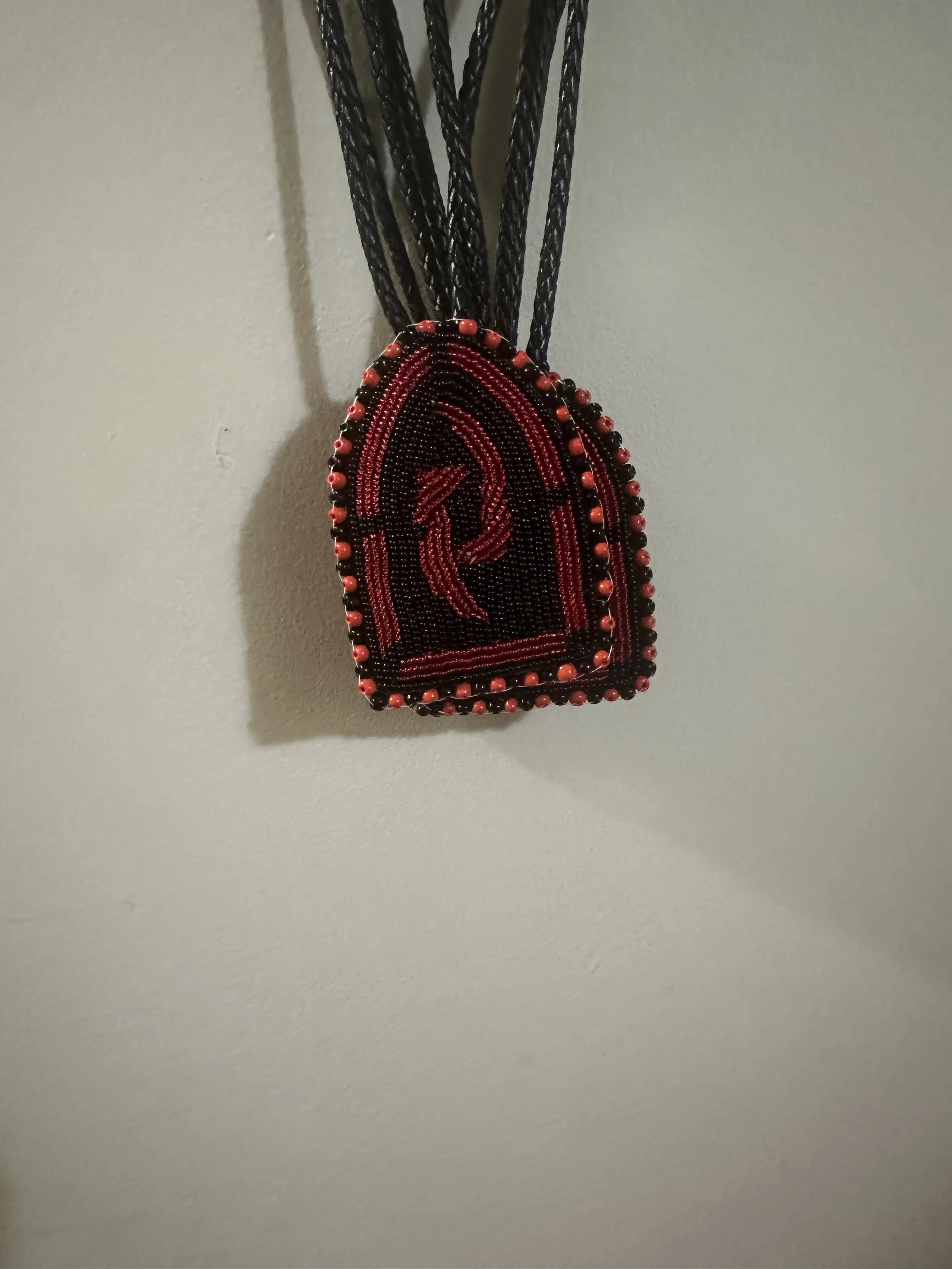 A beaded necklace with black, red, and orange beads hanging on a light-colored wall.