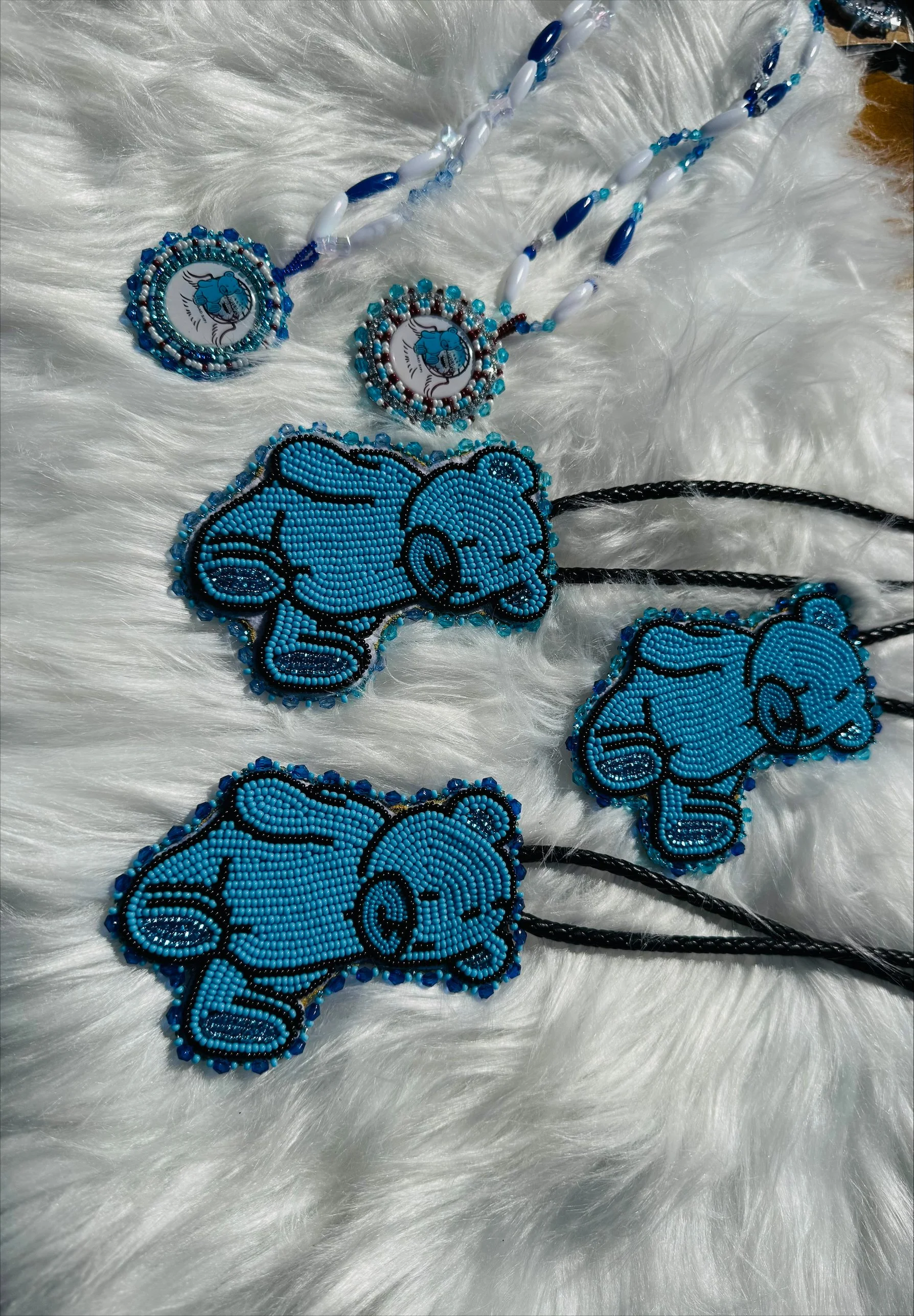 Beaded necklaces with a design of a blue elephant on a white background, placed on a white furry fabric surface.