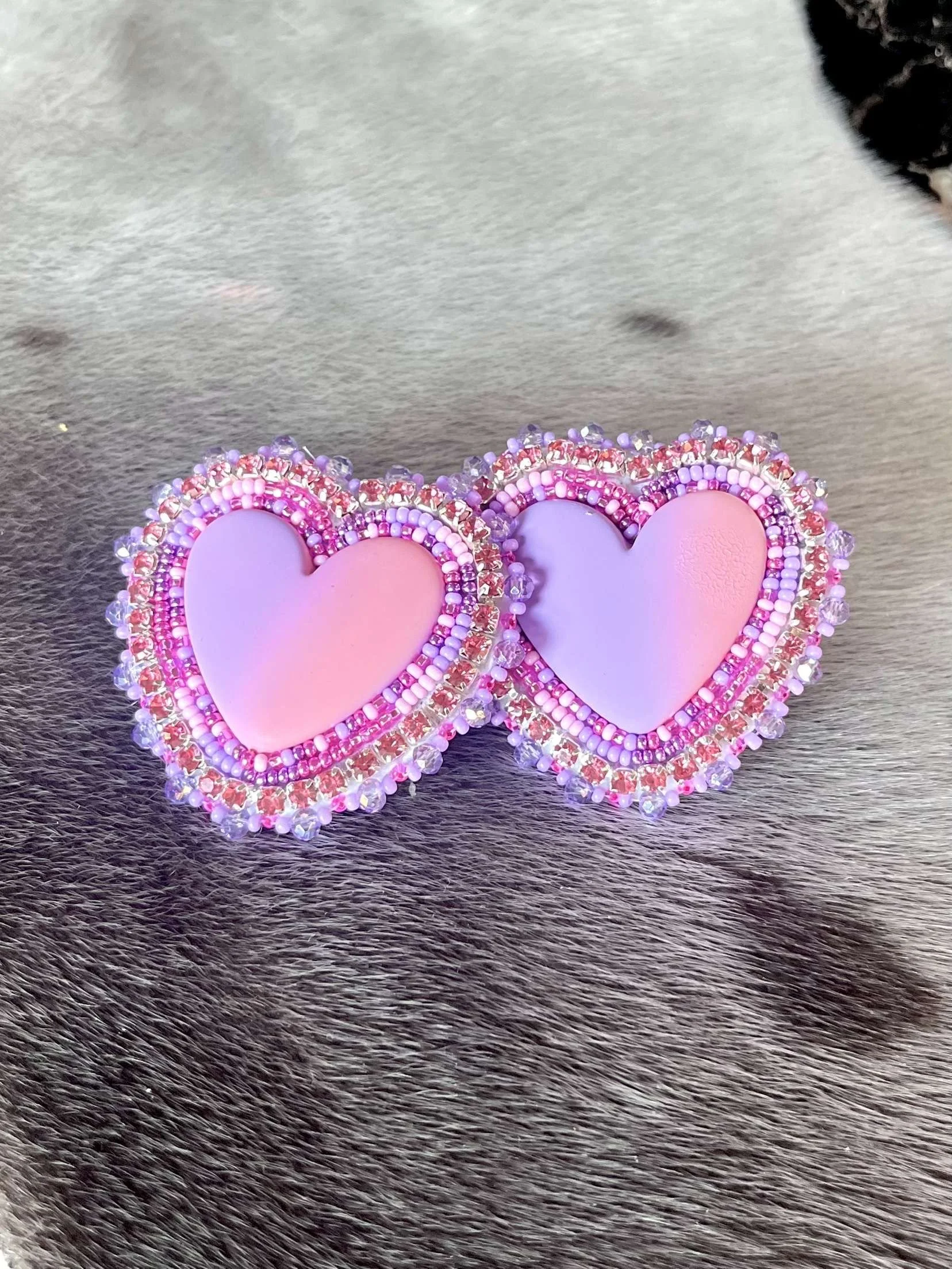 Pair of pink and purple heart-shaped earrings with bead decorations on a furry gray surface.