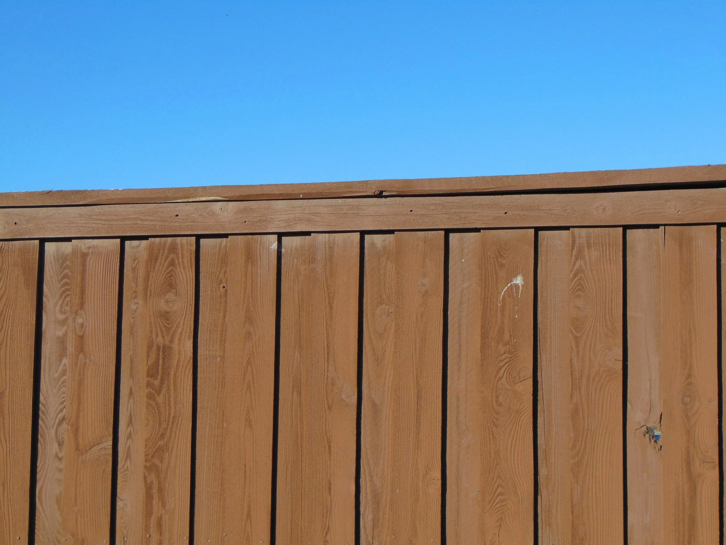 Close-up view of a wooden privacy fence with vertical planks, set against a clear blue sky.