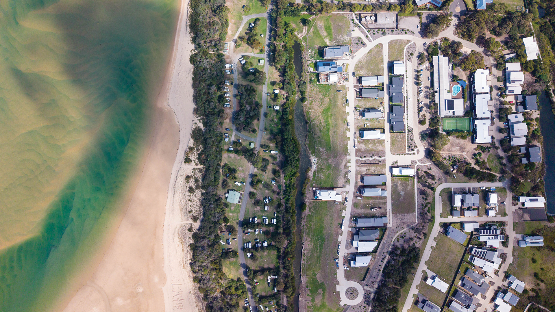 Aerial view of a beach alongside a forested area and residential community.