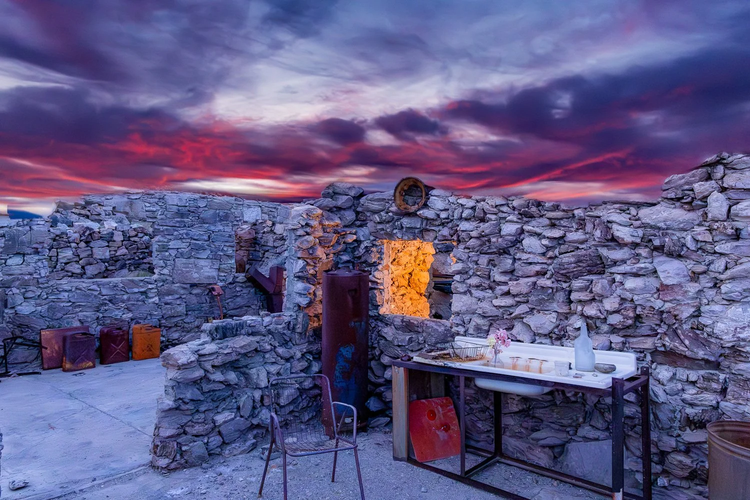 Stone ruins of the Gold Eye Mine with a glowing orange window against a dramatic purple sunset sky.