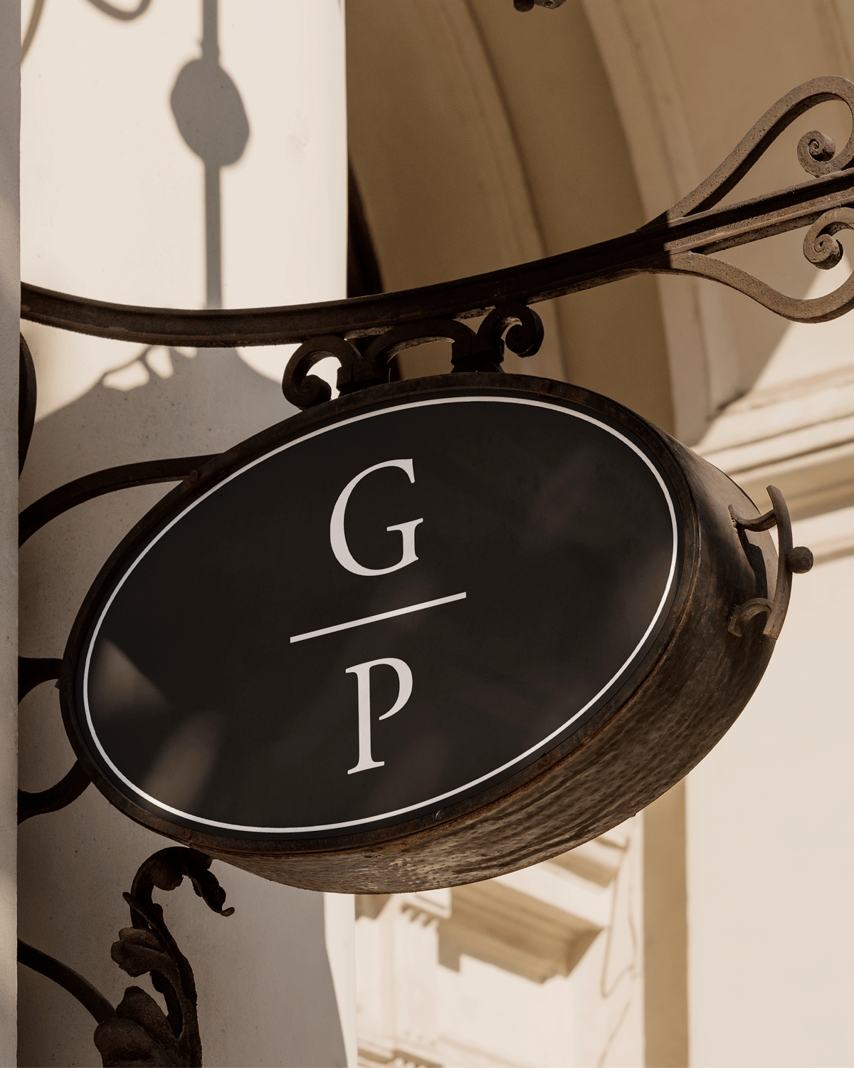 Marketing design for Georgetown Pilates. A black oval sign with white lettering that reads G P, attached to a decorative wrought iron bracket on a building exterior.