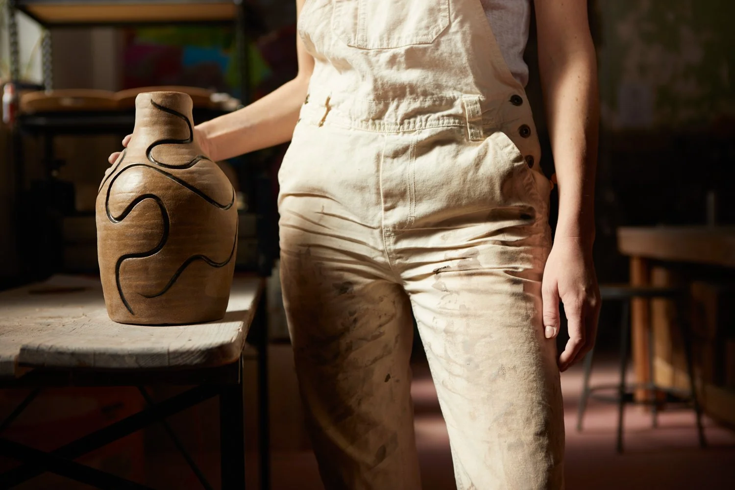 Sarah Stevens standing next to a pottery piece on a table in a studio.