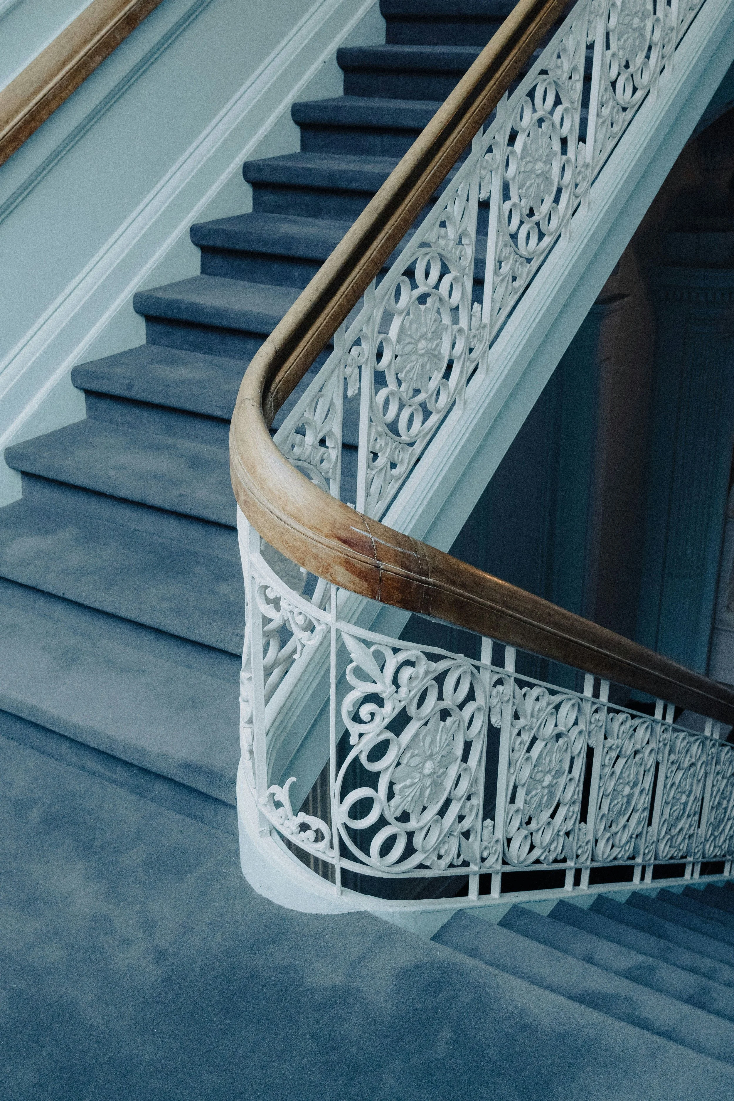 A staircase with a dark blue carpet, a polished wooden handrail, and a white ornate metal railing. Inspiration for Cypress Works General Contracting in Massachusetts.