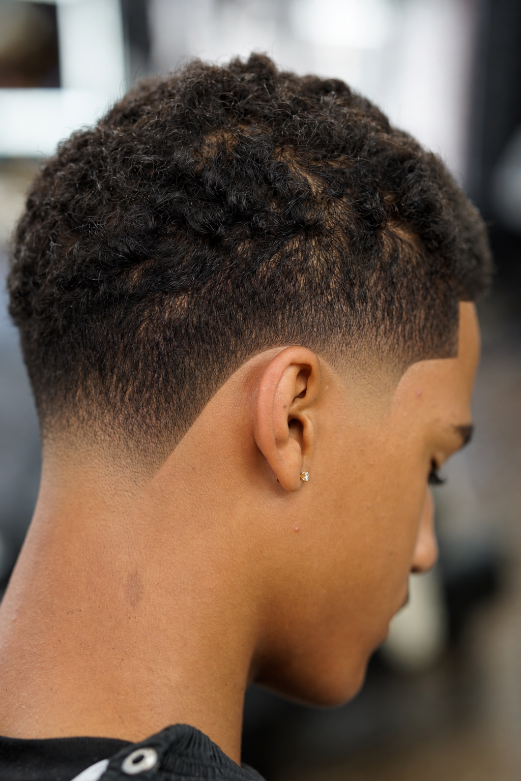Close-up of a person's head with a curly fade haircut and an earring in the left ear.