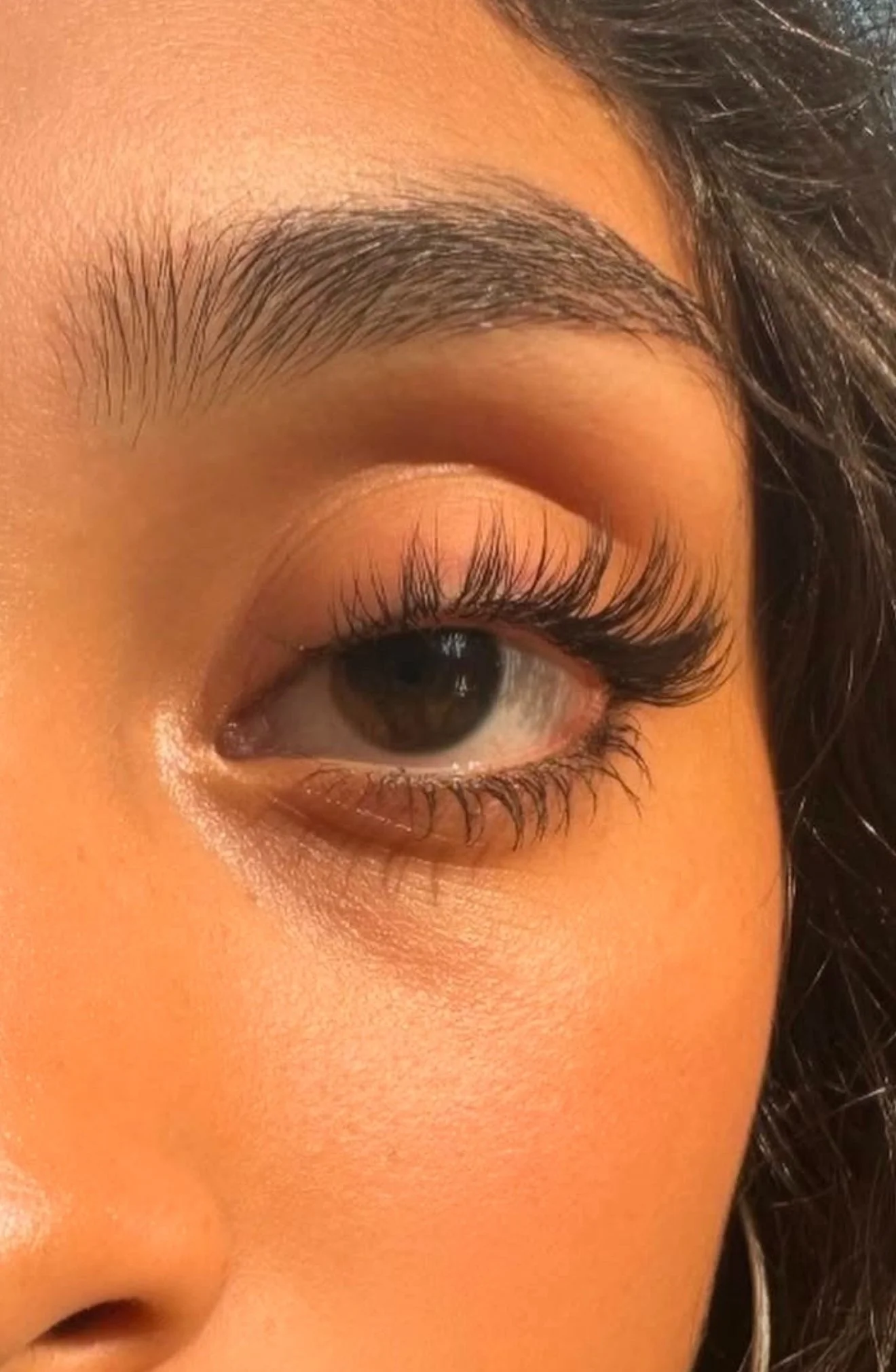 Close-up of a person's eye, eyebrow, and surrounding skin, with dark hair visible on the right side of the image.