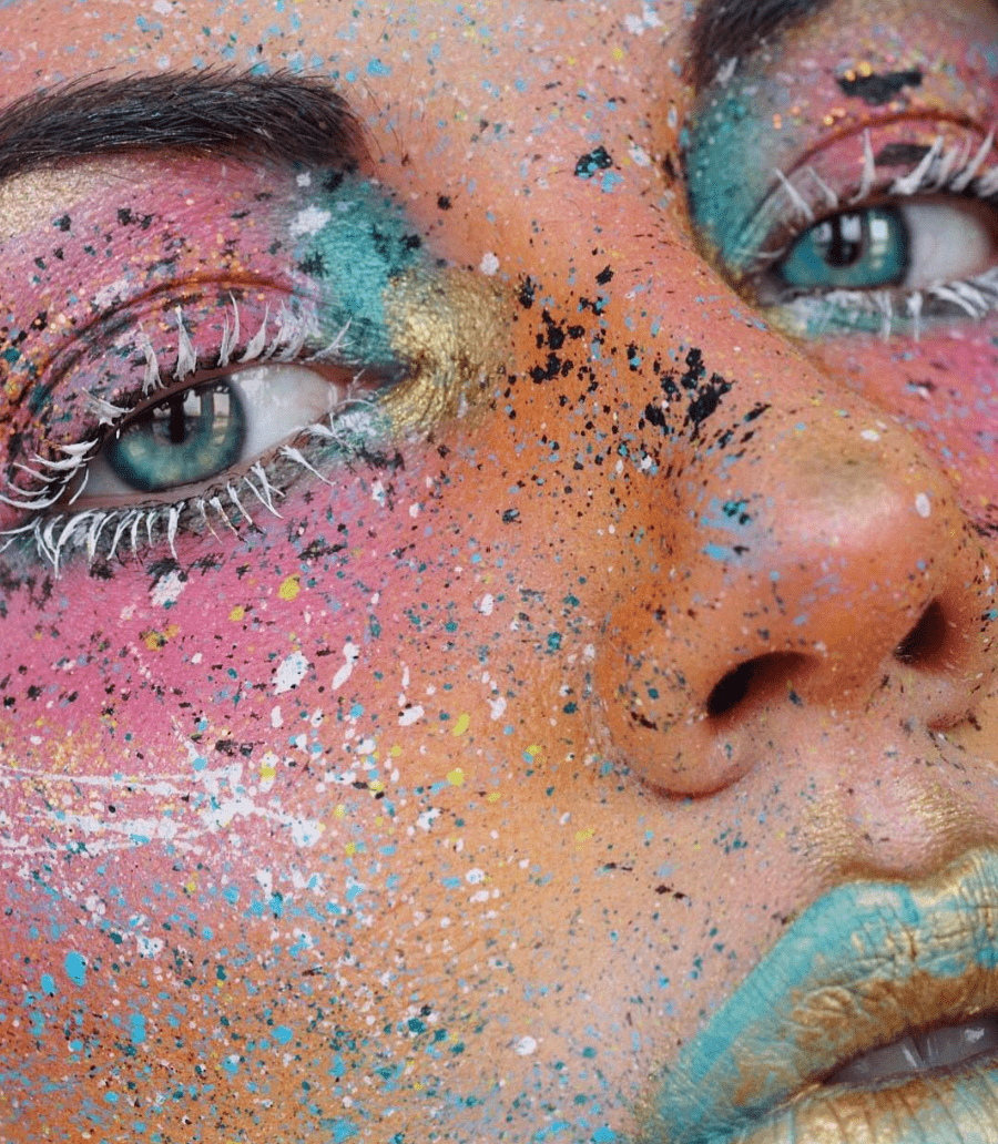 Close-up of a person's face with colorful, speckled face paint and artistic makeup, highlighting the eyes and lips.