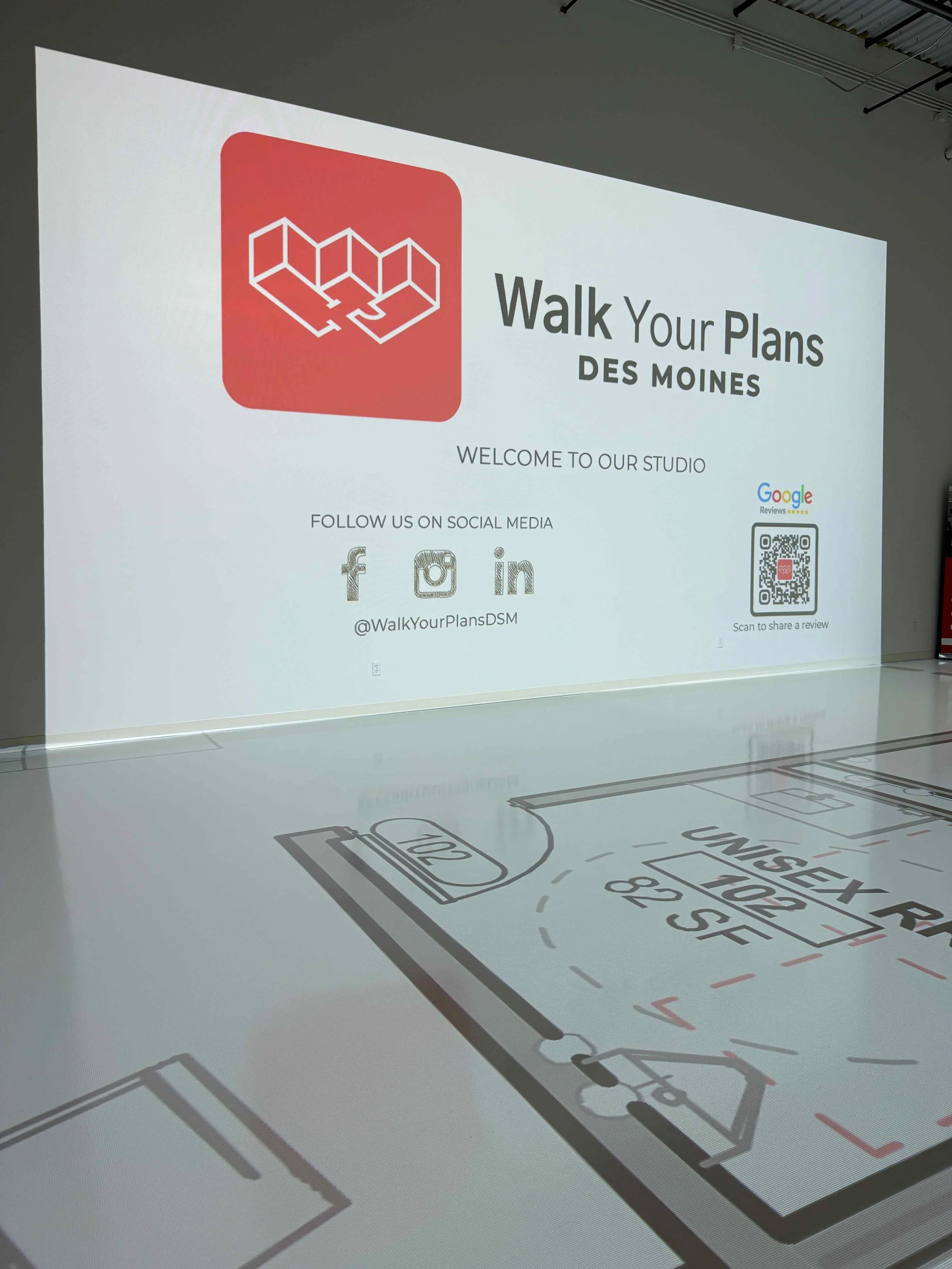 A presentation screen displaying information for 'Walk Your Plans DES MOINES' with social media icons for Facebook, Instagram, and LinkedIn, and a QR code for sharing reviews at an indoor sports facility.