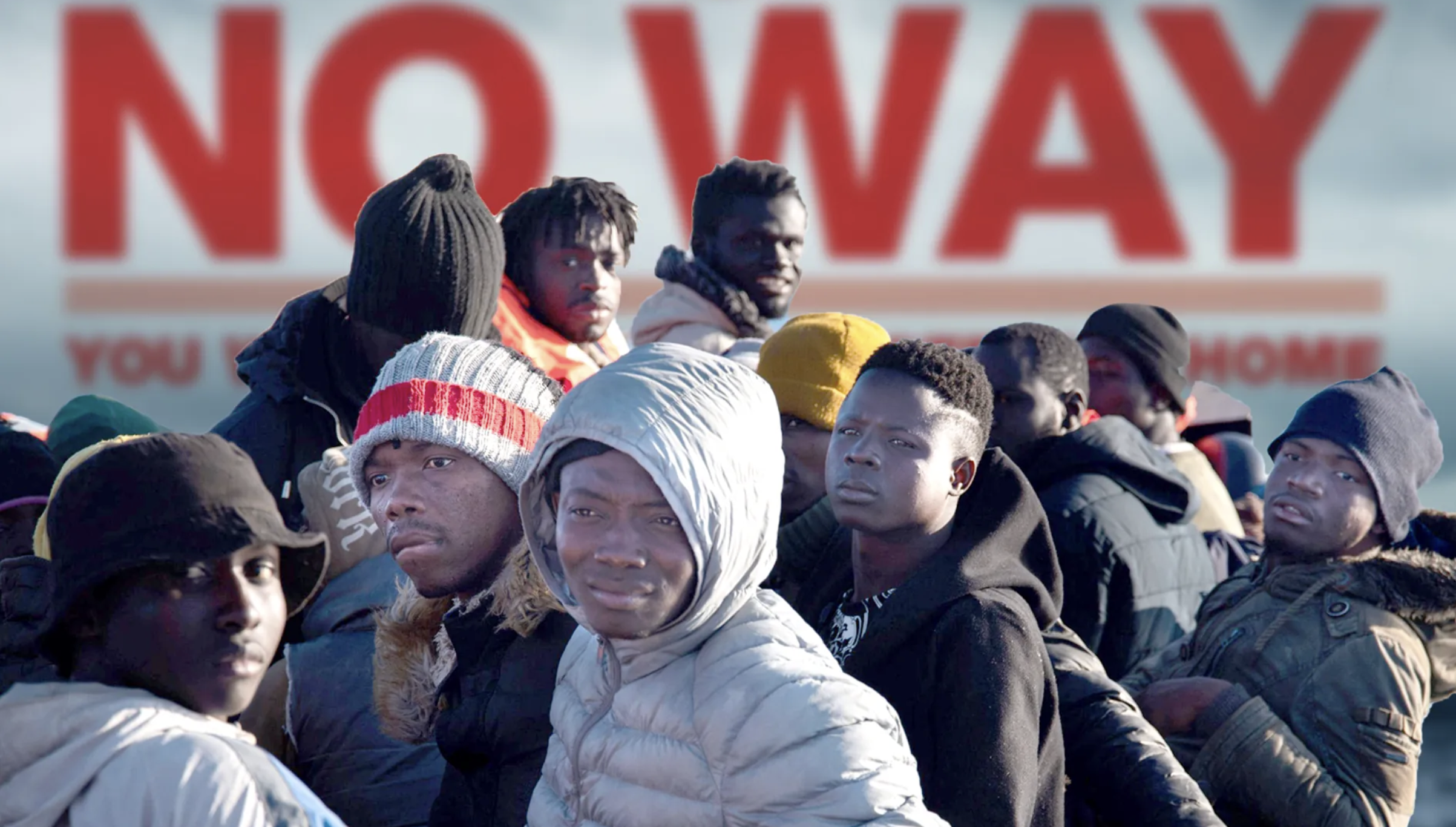 Group of migrants standing in front of a sign that says 'NO WAY.