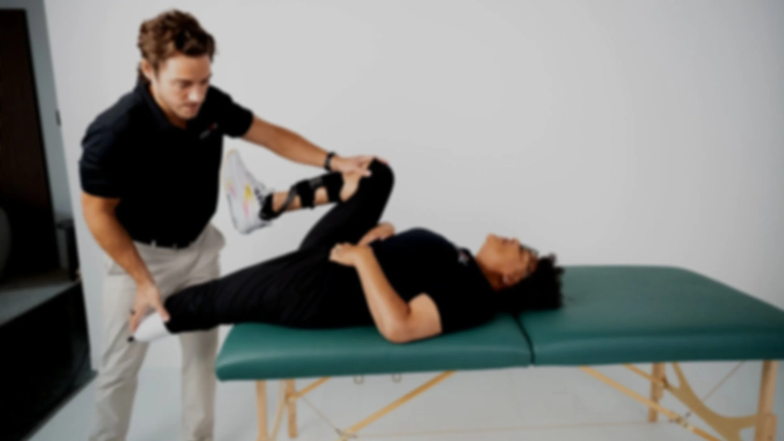 A physical therapist assisting a woman with leg exercises on an examination table in a medical setting.