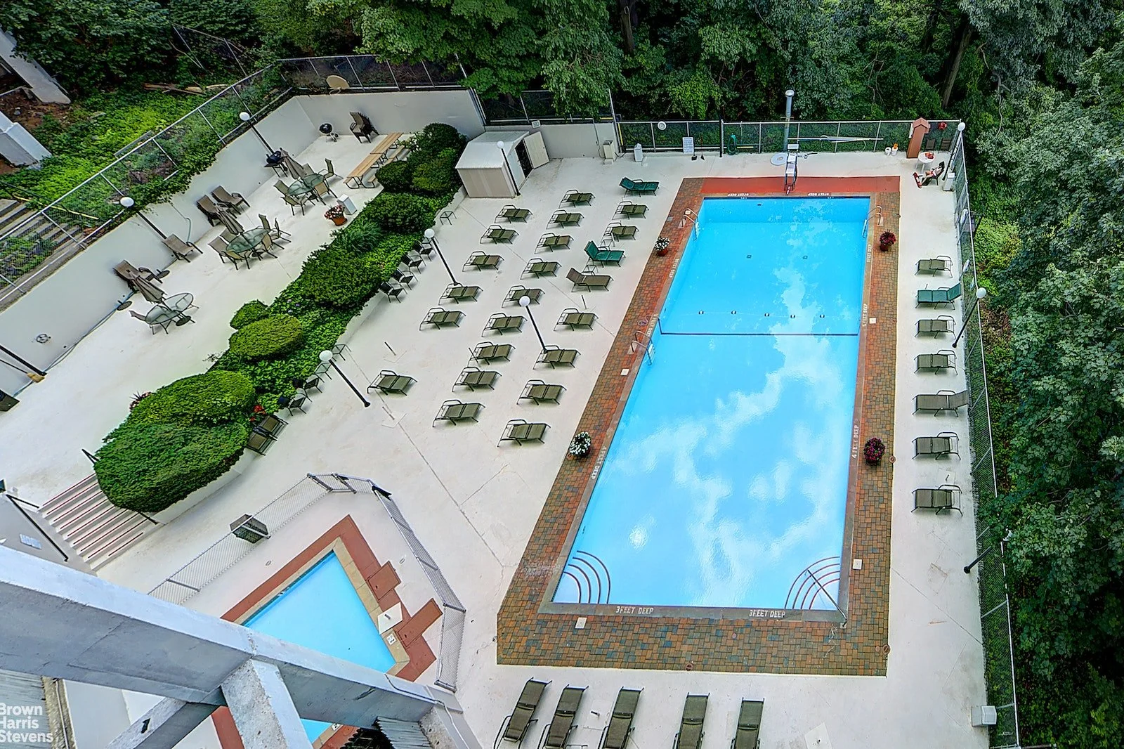 Aerial view of an outdoor swimming pool area with lounge chairs and greenery, surrounded by trees.