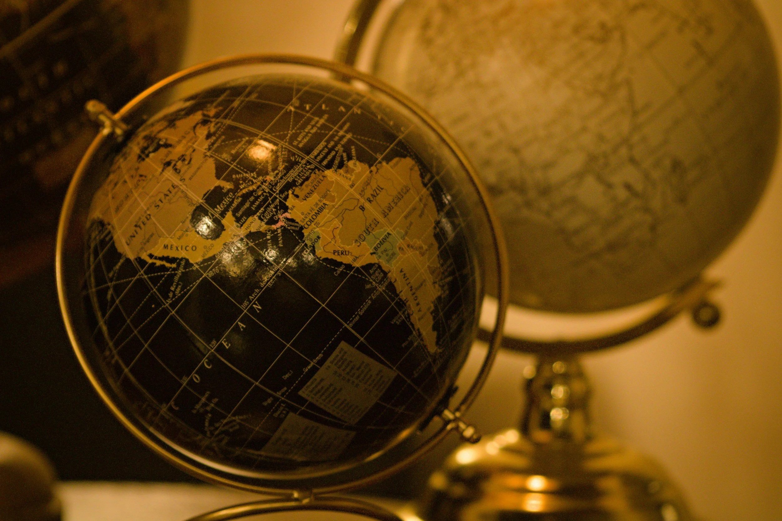 Two Globes of the Earth. The one in front is showing the Western Hemisphere with North, Central, and South America. The one in back is a bit fuzzy showing Eastern Hemisphere. Metaphor for growing in connection, holistic health, and accurate health ed