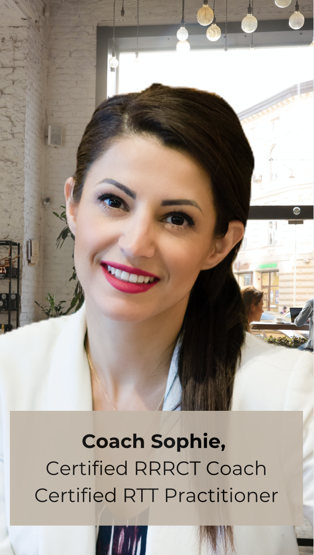 A woman with dark brown hair smiling, wearing a light-colored blazer, seated in a cafe with large windows and hanging light bulbs in the background, for a professional profile or advertisement.