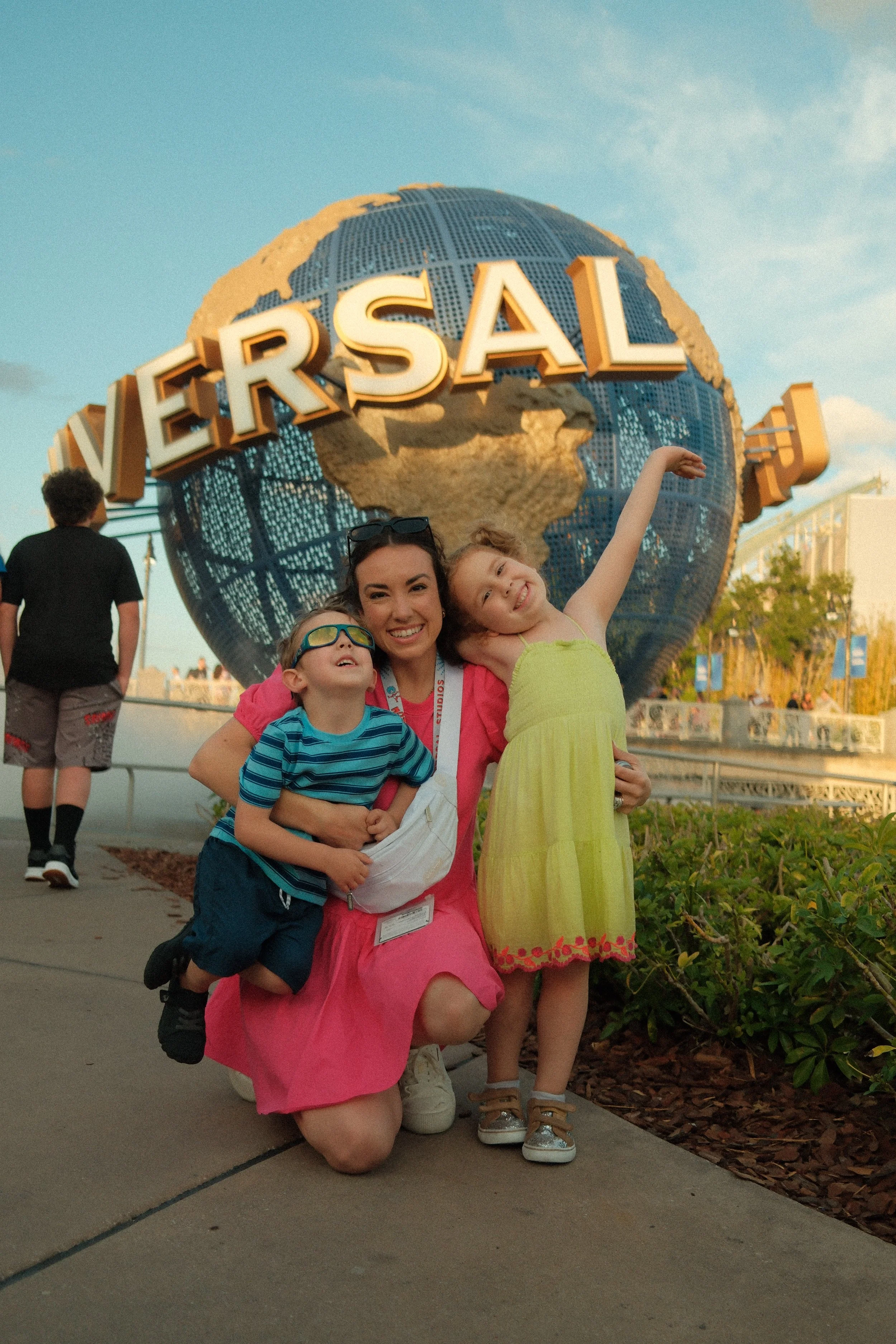 A woman and two children smiling and posing in front of the Universal Studios globe at sunset.