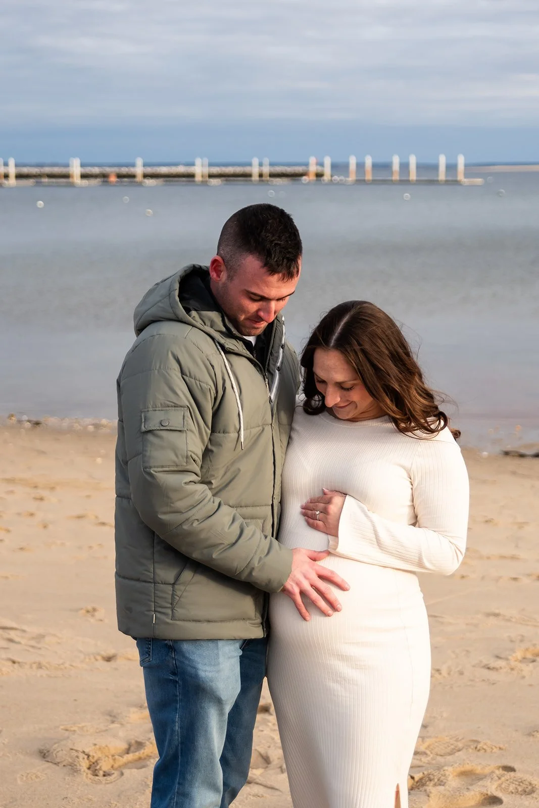 Couple on beach in Provincetown looking down at mama-to-be's belly