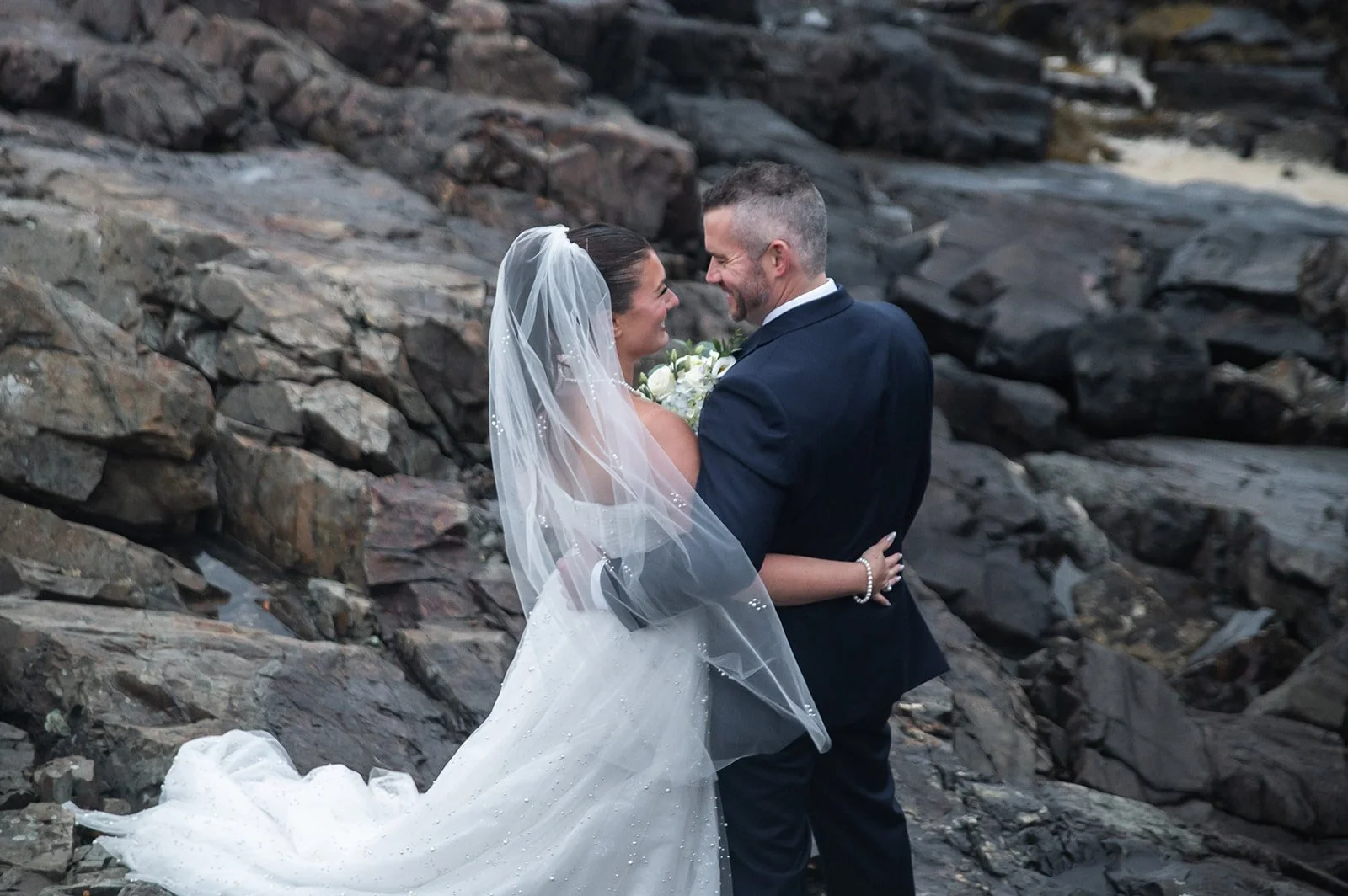 Bride and groom on rocks at the Marginal Way embracing and looking at each other lovingly