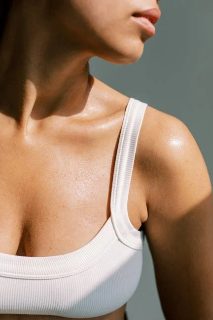 Close-up of a woman's shoulder and neck, wearing a white tank top.