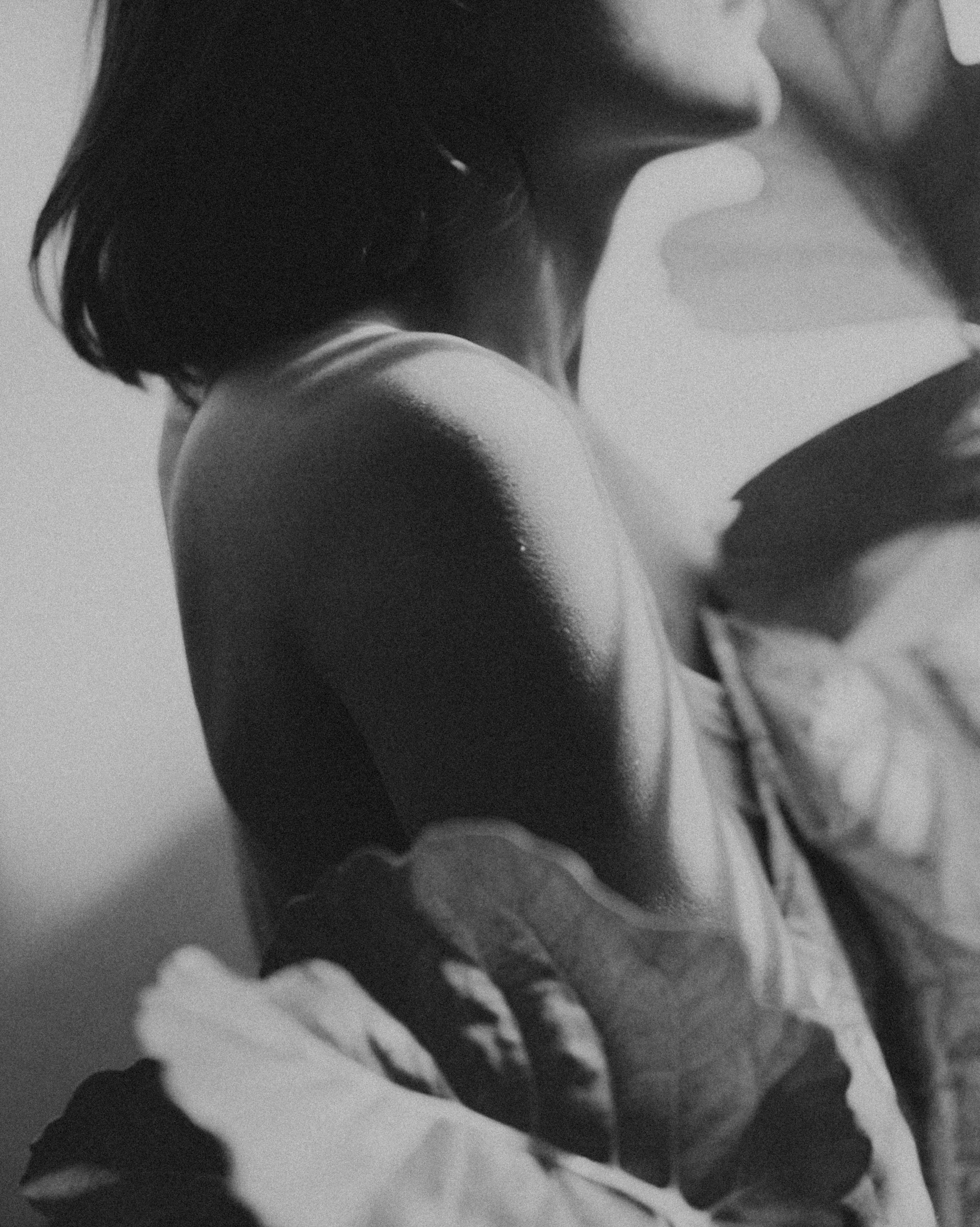 A black and white close-up photo of a woman hugging herself, showing her shoulder, arm, and part of her face with short hair.
