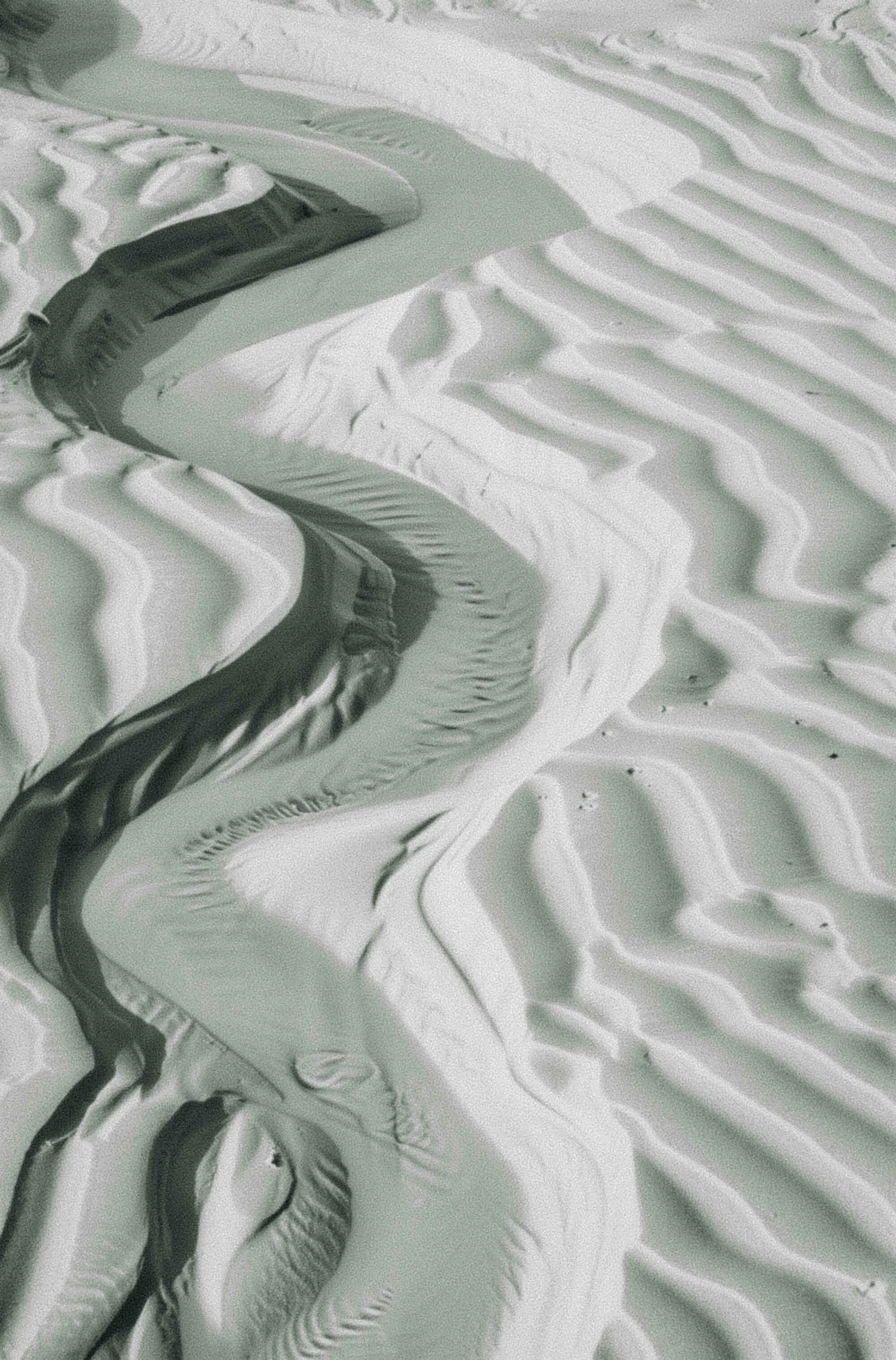 Close-up of sand dunes and a river flowing through the landscape with pattern and texture in the sand.