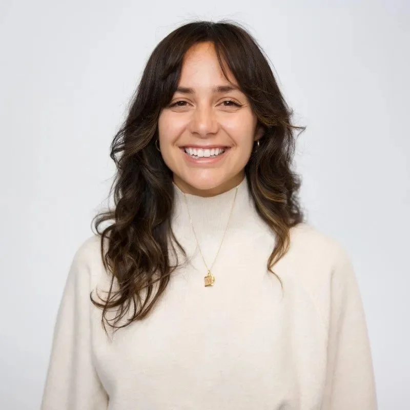 Woman smiling in beige sweater with long dark hair and necklace
